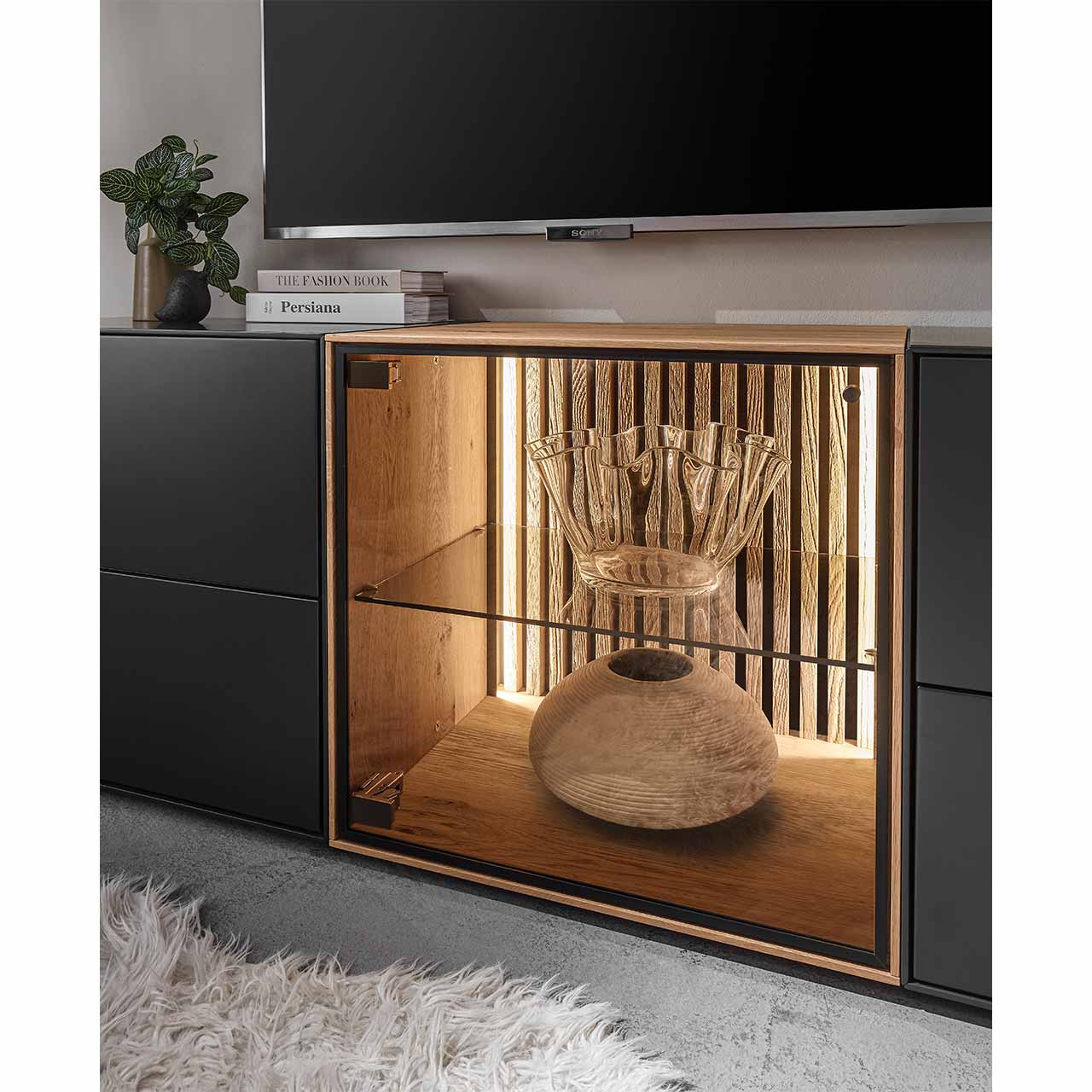 Detailaufnahme einer quadratischen Lowboard-Vitrine aus hellem Holz mit beleuchteter Lamellenrückwand und Glaseinlegeboden - Bildausschnitt aus Wohnwand.