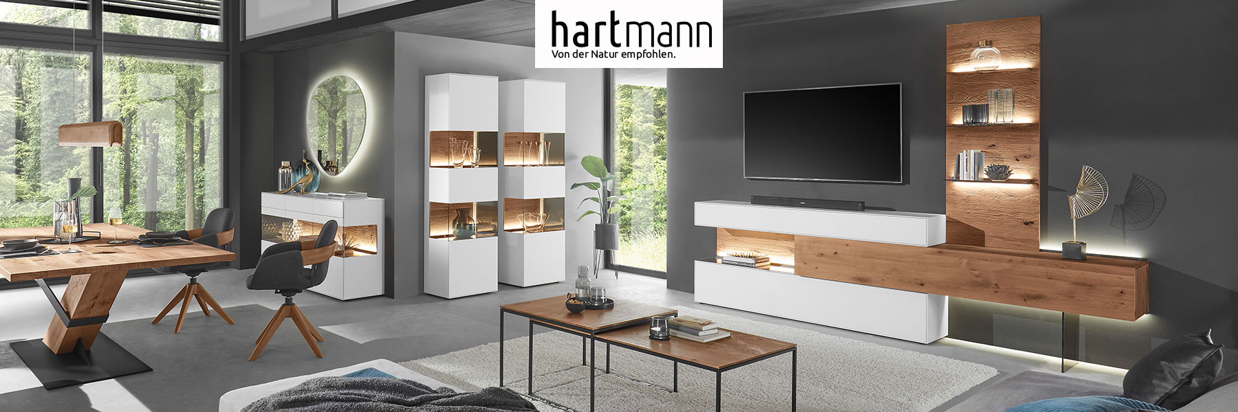 Hartmann TORIDO - Moderne Möbel aus massiver Birke weiß lackiert kombiniert mit Kerneiche Umato. Ambientebild zeigt Wohn - und Essbereich mit Wohnwand, Couchtisch, Standvitrinen, Sideboard sowie passendem Esstisch mit Stühlen.