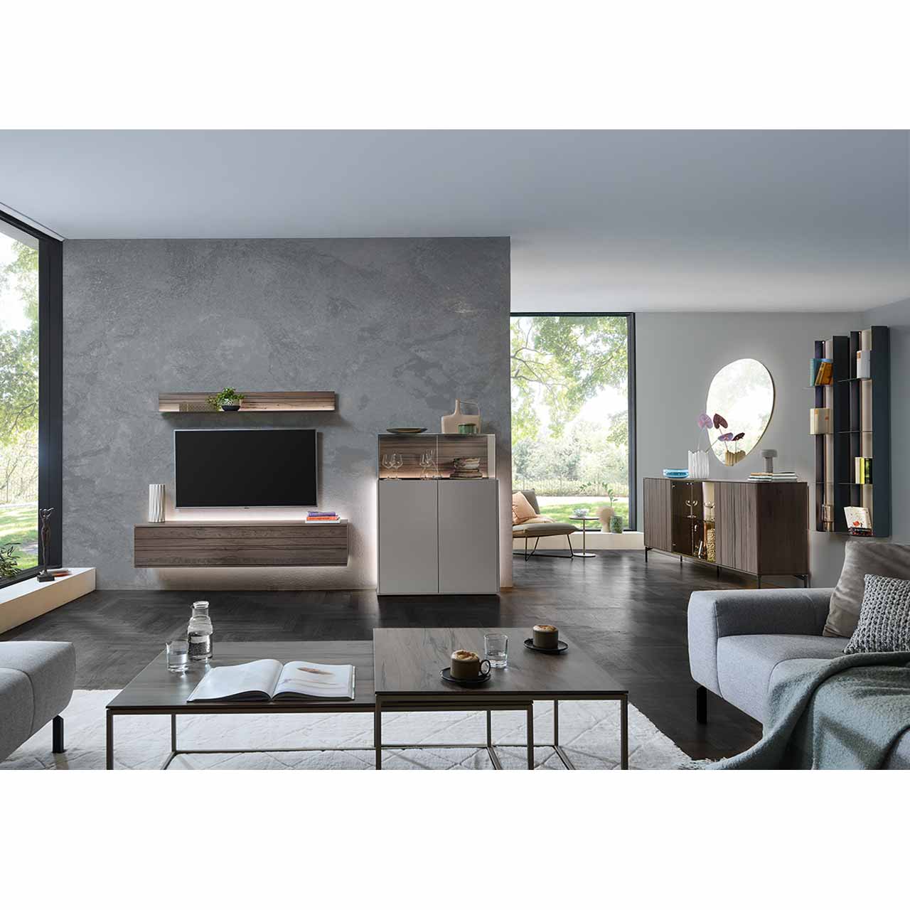 Milieubild - Hartmann AUDRA 5610 - Wohnzimmermöbel aus Altholzbuche Uyaa und Lack Sand Modernes Wohnzimmer mit dreiteiliger Wohnwand bestehend aus Hängelowboard und Wandregal in dunkelbraunem Holz mit Maserung, daneben Highboard in Lack Sand mit aufgesetztem Glaskasten. Rechts an der Wand das passende Sideboard und zwei Metallregale.