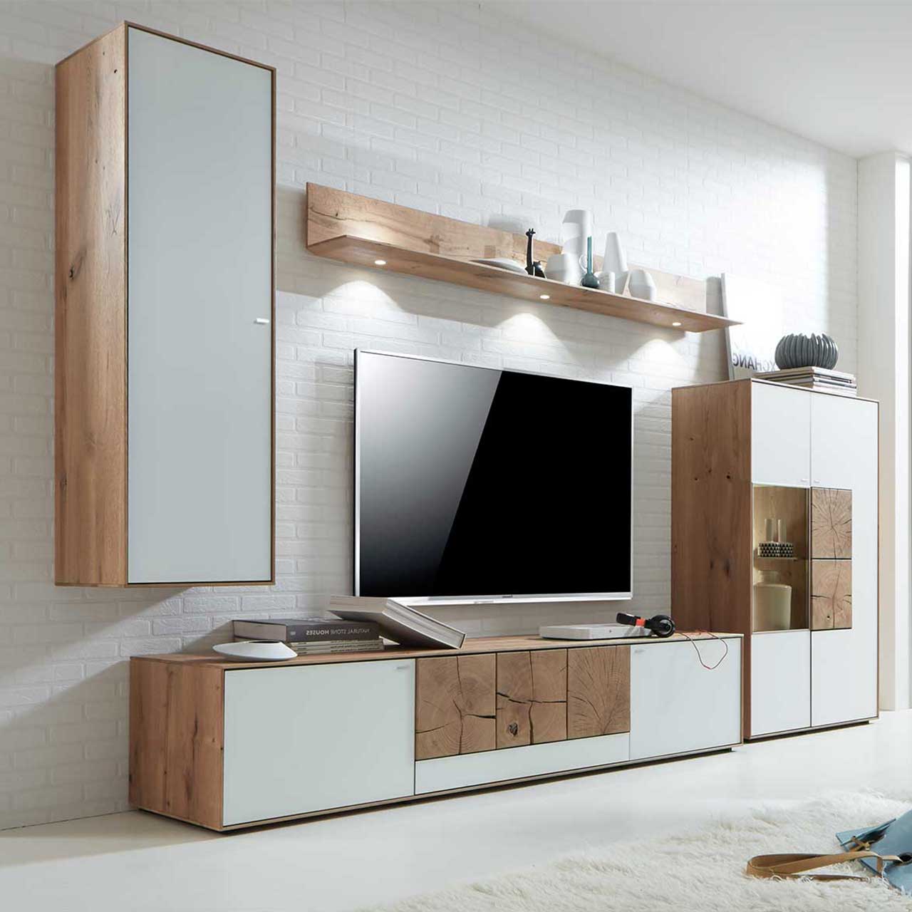Milieubild Hartmann CAYA - Hängeelement 7170-7045W li. - Türanschlag links Wohnzimmer mit TV und moderner Massivholz Wohnwand aus Kerneiche Umato mit Mattglas weiß Fronten und rechteckigen Hirnholzscheiben: Hängeschrank, beleuchtetes Wandregal, Lowboard mit Hirnholz, Highboard mit Glasausschnitt und Hirnholz.