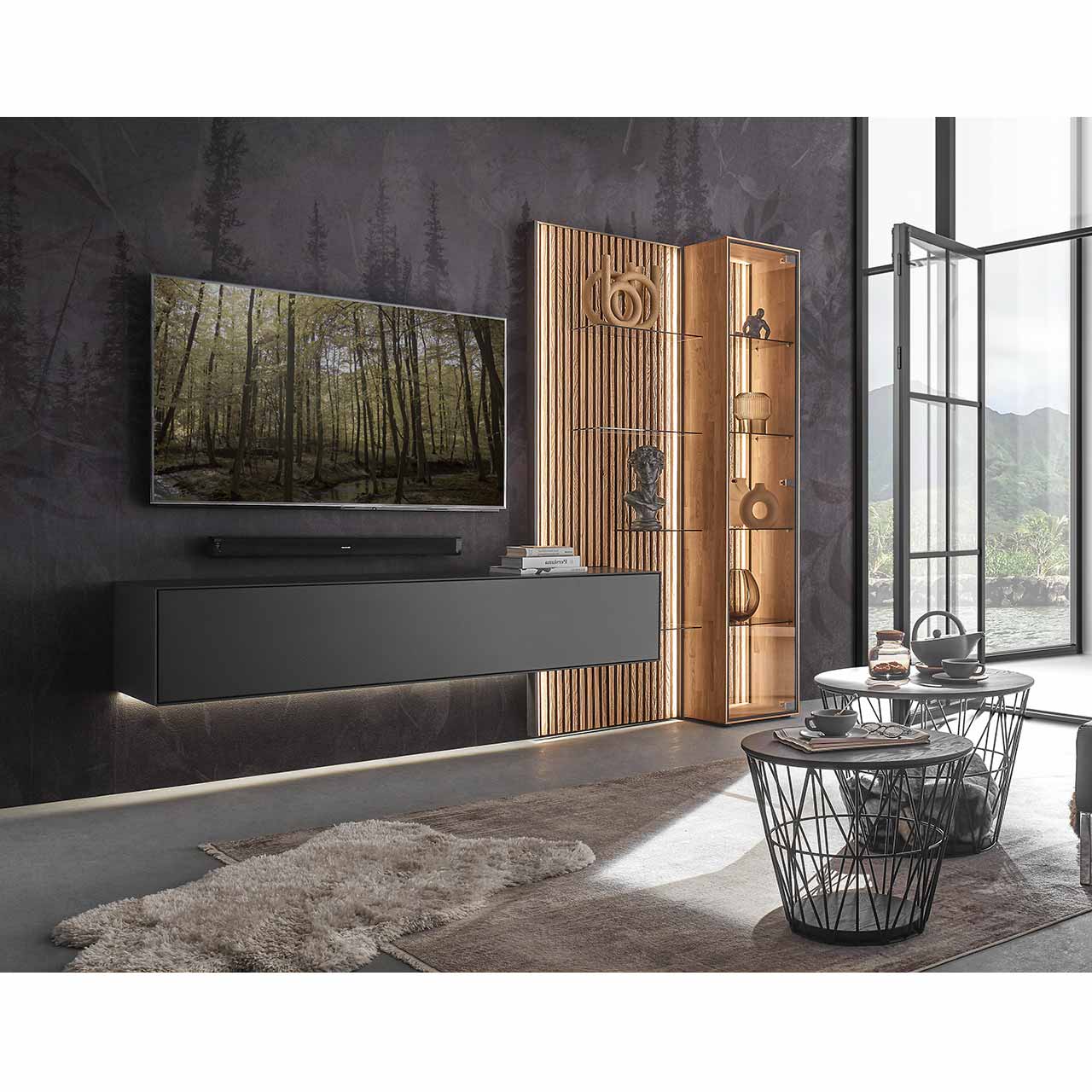 Modernes Wohnzimmer mit Fernseher und moderner dreiteiliger Wohnwand aus massivem Holz: Ein schlichtes Hängelowboard anthrazit lackiert, eine Standvitrine und ein Wandpaneel mit hellen Holzlamellen und Glas – vor dunkelgrauer Wand.