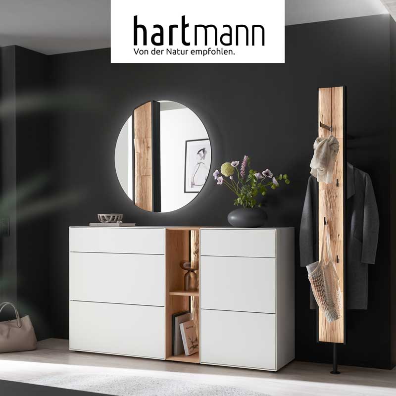 Hartmann SALVO - Flurmöbel aus massiver Kerneiche Natur und Birke weiß lackiert kombiniert mit Akzenten aus echter Baumrinde, Holzlamellen oder Spaltholz. Ambientebild zeigt zwei weiße Stauraumschränke, runden Wandspiegel und eine Wandgarderobe.