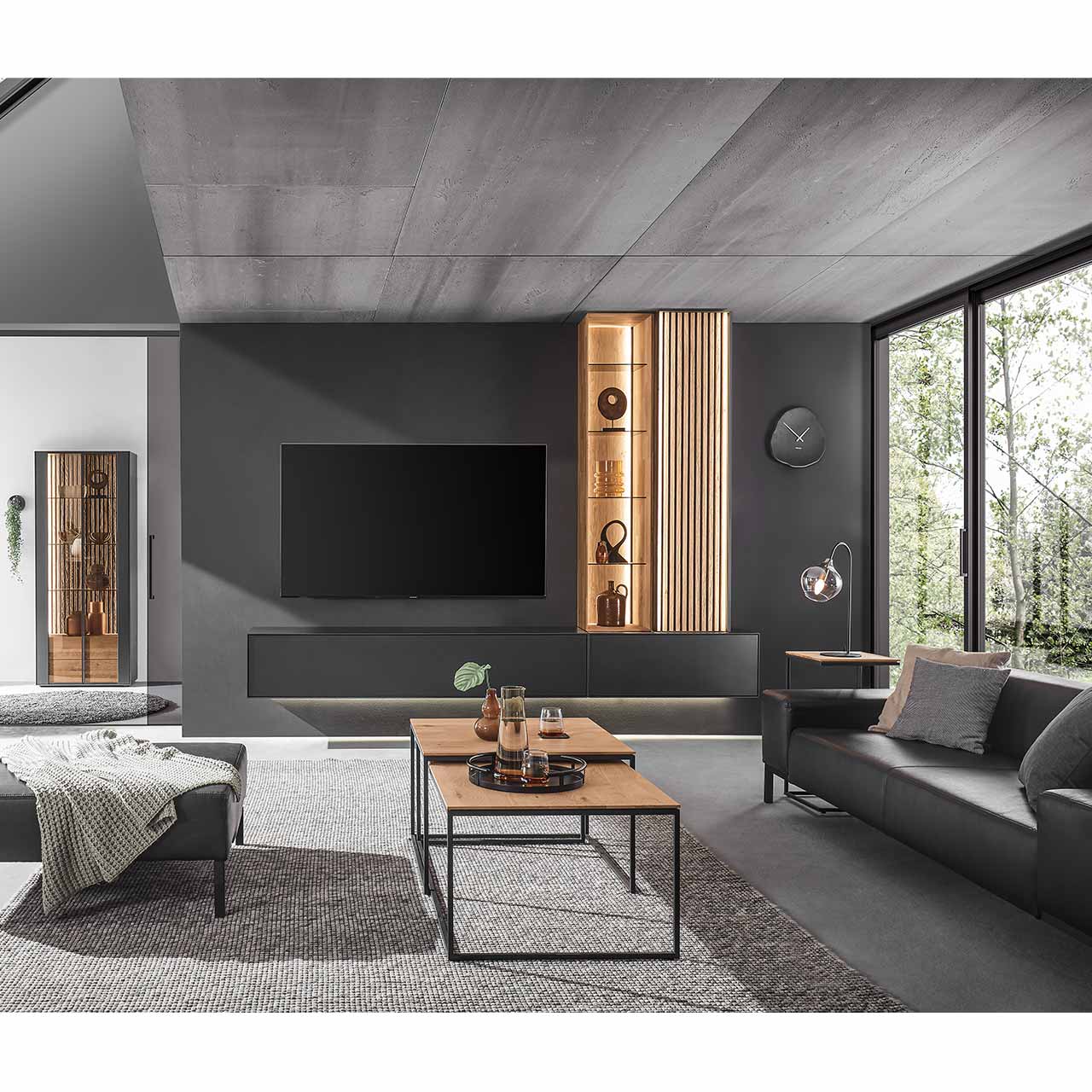 Wohnzimmer mit moderner, vierteiliger Wohnwand in Anthrazit kombiniert mit hellem Holz und Lamellen: Hängelowboard anthrazit, Hängevitrine und Hängeschrank mit Lamellen in heller Kerneiche, davor zwei filigrane ineinander geschobene Couchtische.