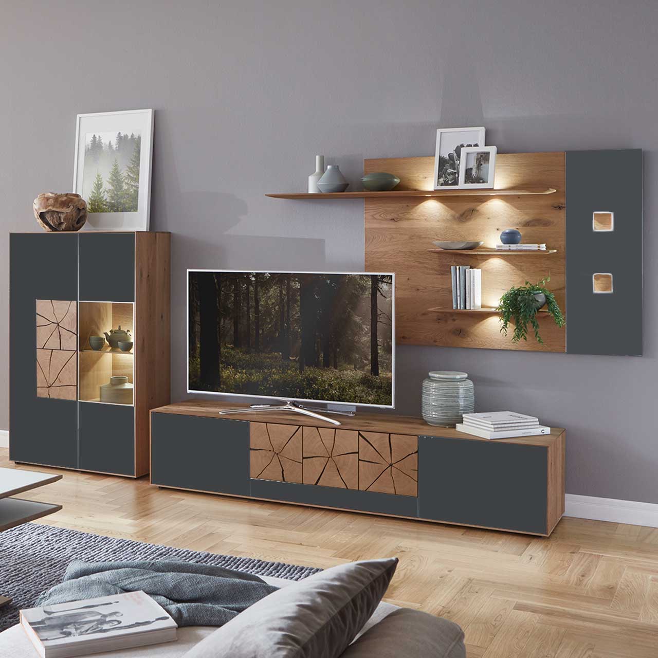 Wohnzimmer mit moderner dreiteiliger Massivholz Wohnwand mit Mattglas Anthrazit Fronten und dekorativen Hirnholzscheiben: Langes Lowboard mit Hirnholz, Wandpaneel mit Regalböden, Highboard mit beleuchtetem Glasausschnitt und Hirnholz.