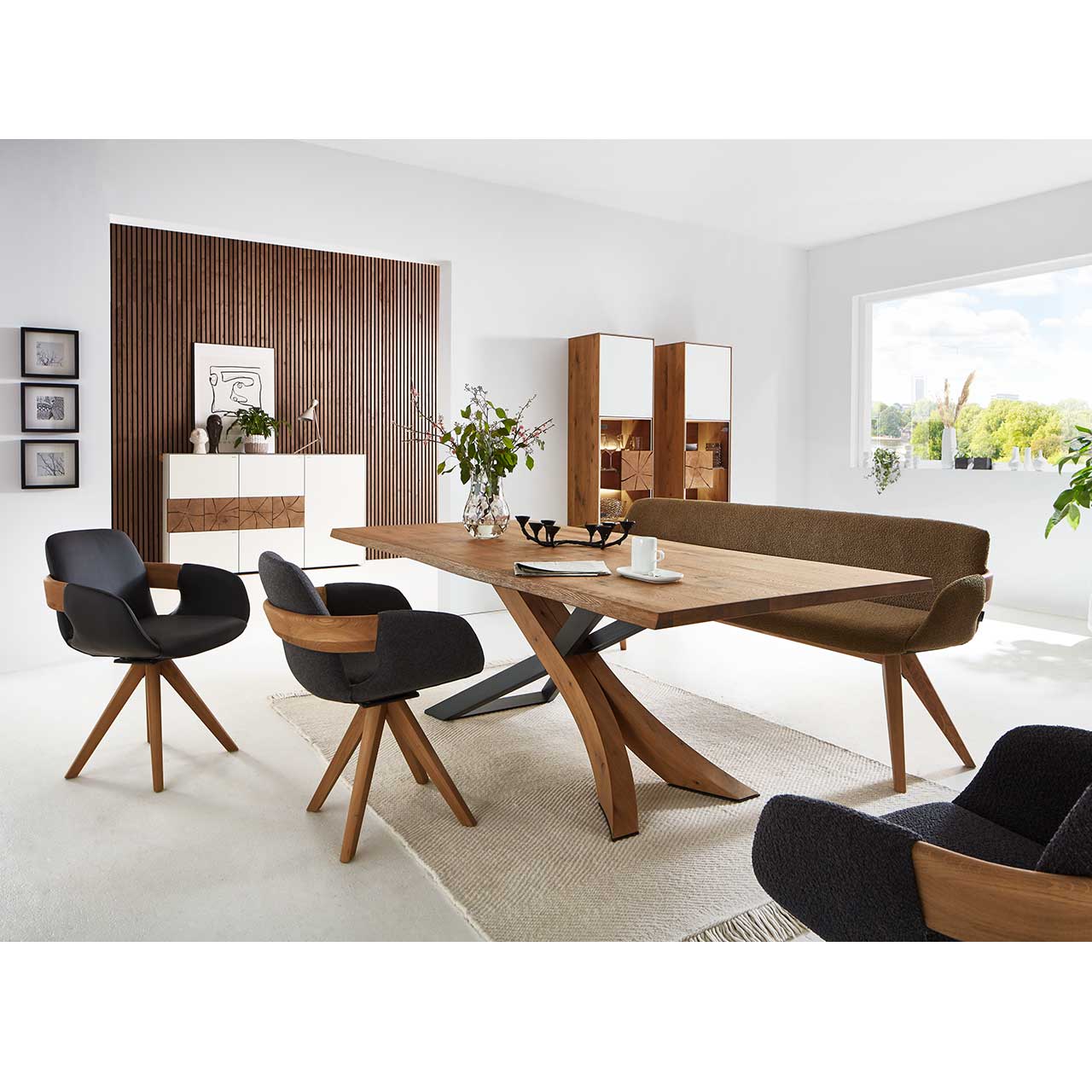 Modernes Esszimmer mit rechteckigem Holztisch, umgeben von drei Stühlen und der passenden Polstersitzbank. Hinten an der Wand stehend die passenden Esszimmermöbel.
