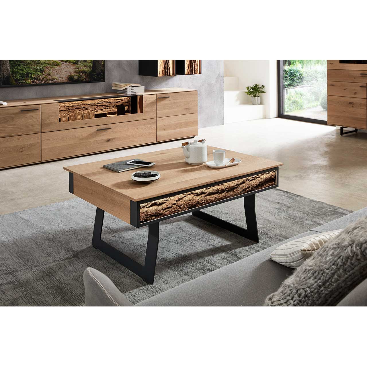 Milieubild Wohnzimmer - Hartmann NATURWERKE - Couchtisch 8400C-1410 Im Wohnzimmer stehender Couchtisch mit höhenverstellbarer Tischplatte aus Kerneiche, integriertem Stauraumfach und seitlicher Rindenapplikation – auf zwei Metallkufen in Anthrazit
