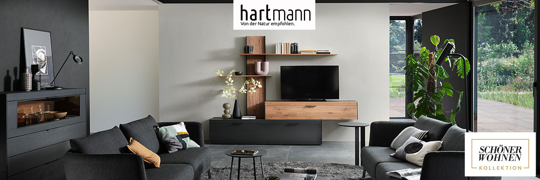 Hartmann Möbel - Möbelserie YORIS Schöner Wohnen Kollektion - Kerneiche Umato Hartmann YORIS - Massivholzmöbel aus Kerneiche Umato kombiniert mit anthrazit gebeizter Eiche und Metall. Ambientebild zeigt eine moderne Wohnwand mit Lowboard, Wandpaneel und Hängeschrank, links passendes Highboard mit Glasklappe.