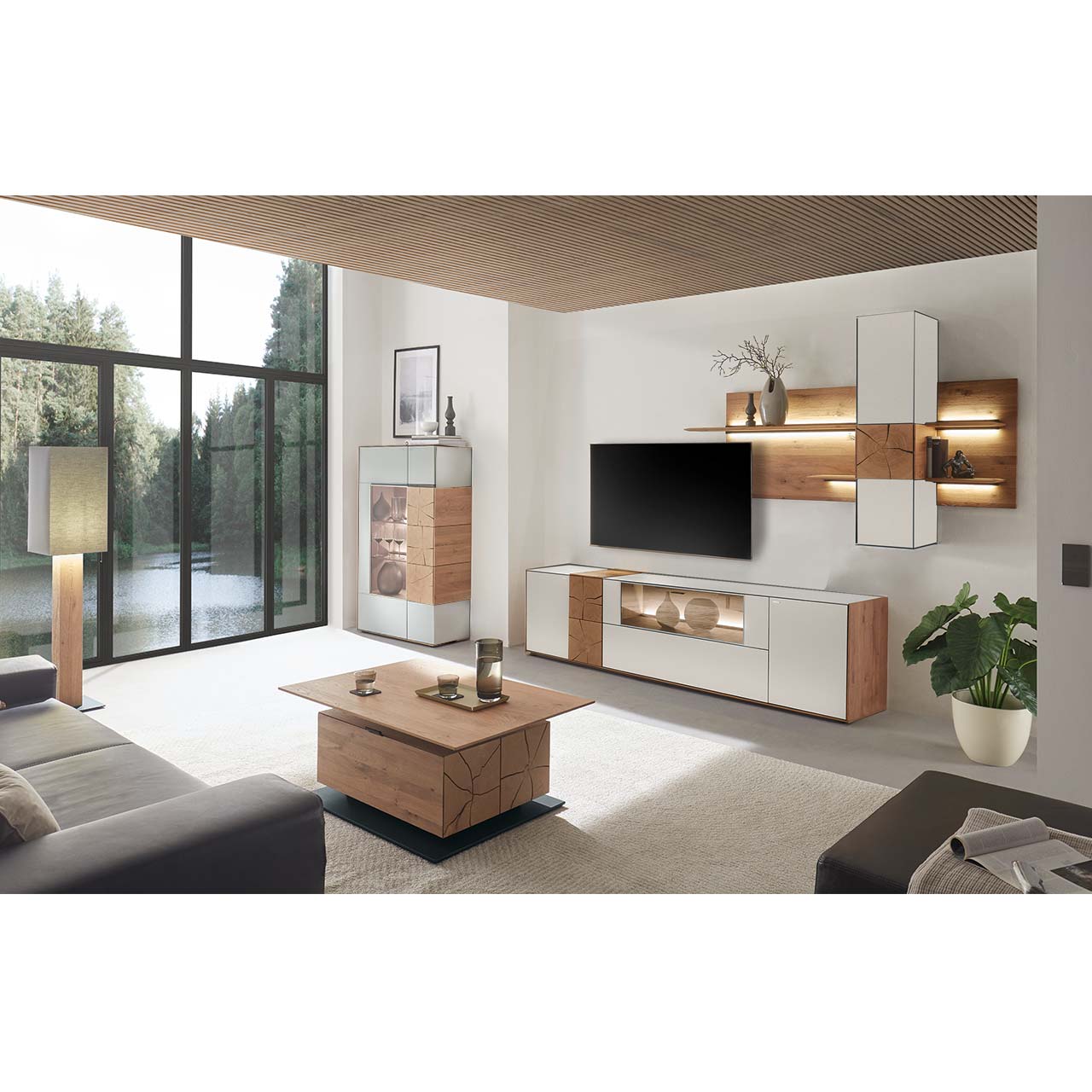 Moderne Wohnwand aus massiver Kerneiche mit Mattglas weißen Fronten, mit Lowboard mit Glasausschnitt sowie Wandpaneel mit Regalböden und Hängeschrank. Links ein Highboard mit Glasfront und Hirnholzscheiben. Im Vordergrund der passende Couchtisch. 