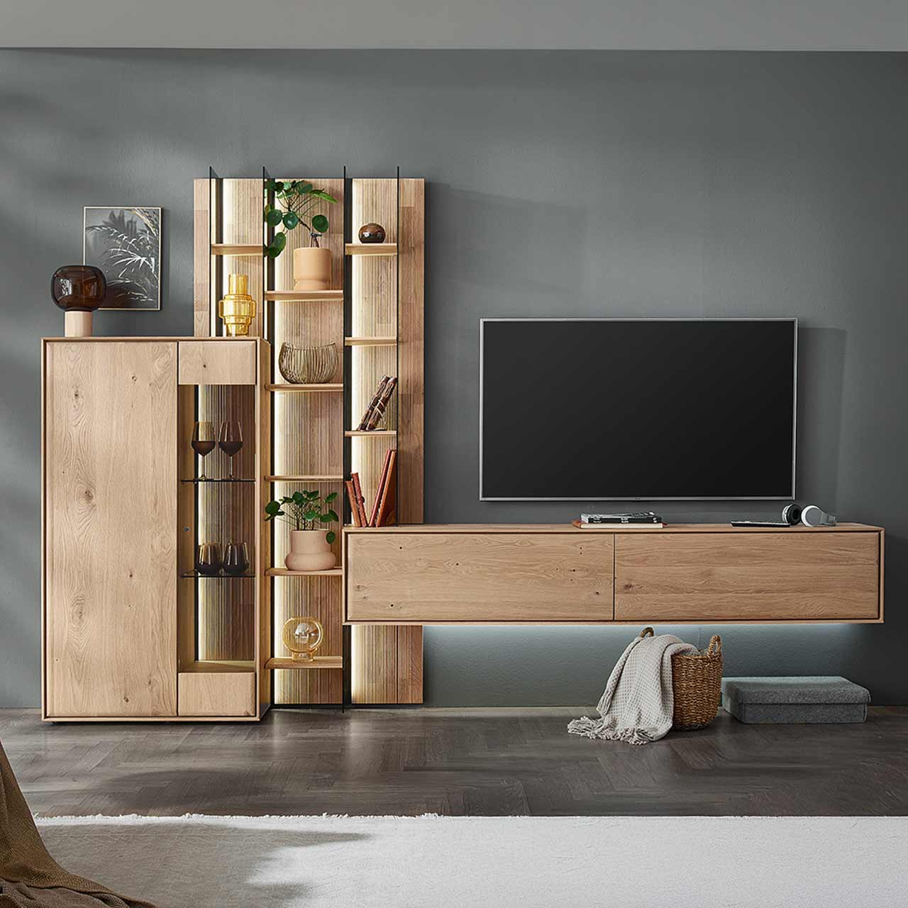 Moderne dreiteilige Wohnwand aus massiver Kerneiche Natur bestehend aus einem Highboard mit Glastür, einem hohen Wandregal mit Holzböden, beleuchteten Glasseiten und geschroppter Rückwand und einem darin integriertem Hängelowboard.