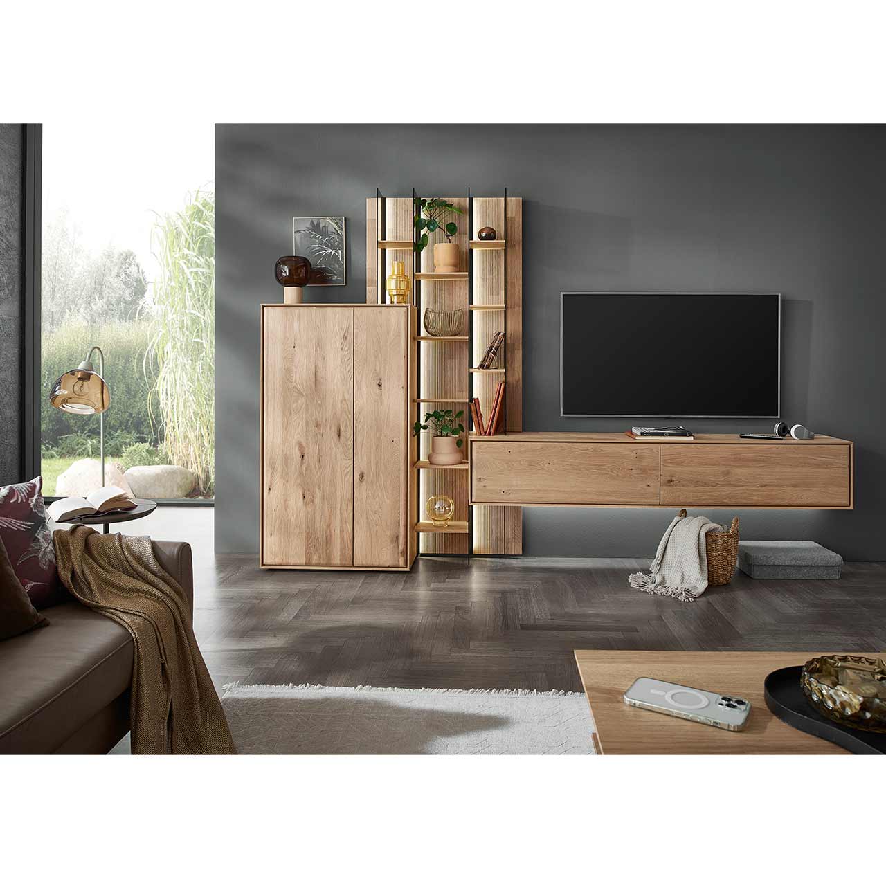 Modernes Wohnzimmer mit dreiteiliger Massivholzwohnwand bestehend aus einem Highboard, einem hohen Wandregal mit Holzböden, beleuchteten Glasseiten und geschroppter Rückwand und einem darin integriertem Hängelowboard. Davor passender Couchtisch.