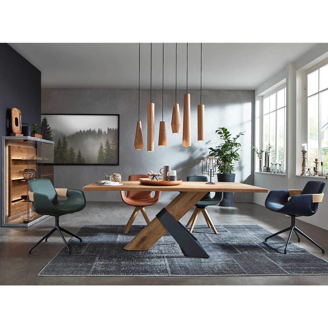 Modernes Esszimmer mit rechteckigem Holztisch umgeben vor vier Stühlen. Darüber hängend eine Pendelleuchte mit sechs unterschiedlichen, zylinderförmigen Holzkörpern aus massiver Kerneiche. 