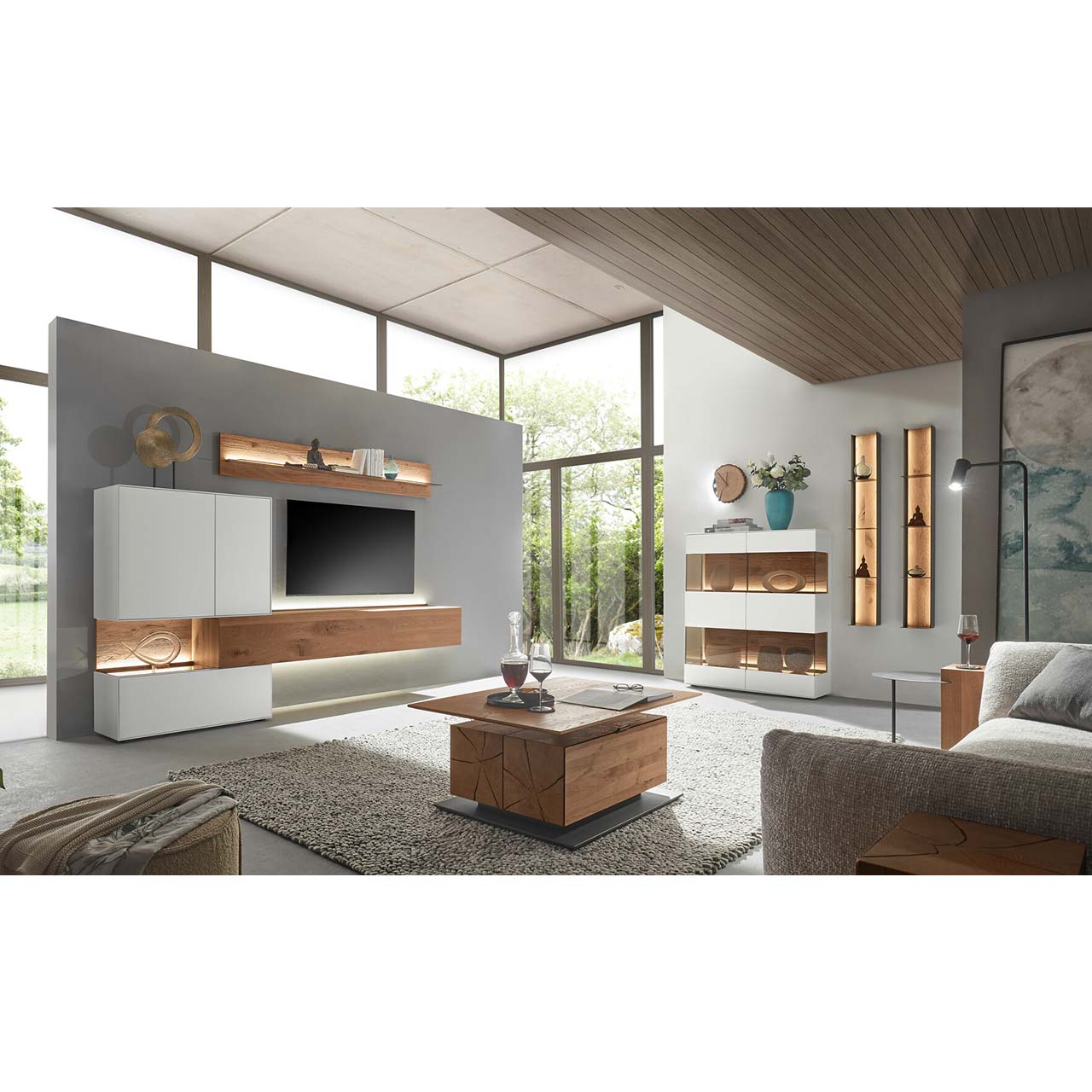 Wohnzimmer mit moderner Wohnwand aus weiß lackierter Birke und dunkler Kerneiche, bestehend aus Hängelowboard, Hänge- und Unterschrank mit Beleuchtung sowie Wandpaneel mit Glasboden. Links ein Highboard mit Metallregalen, davor ein Couchtisch.