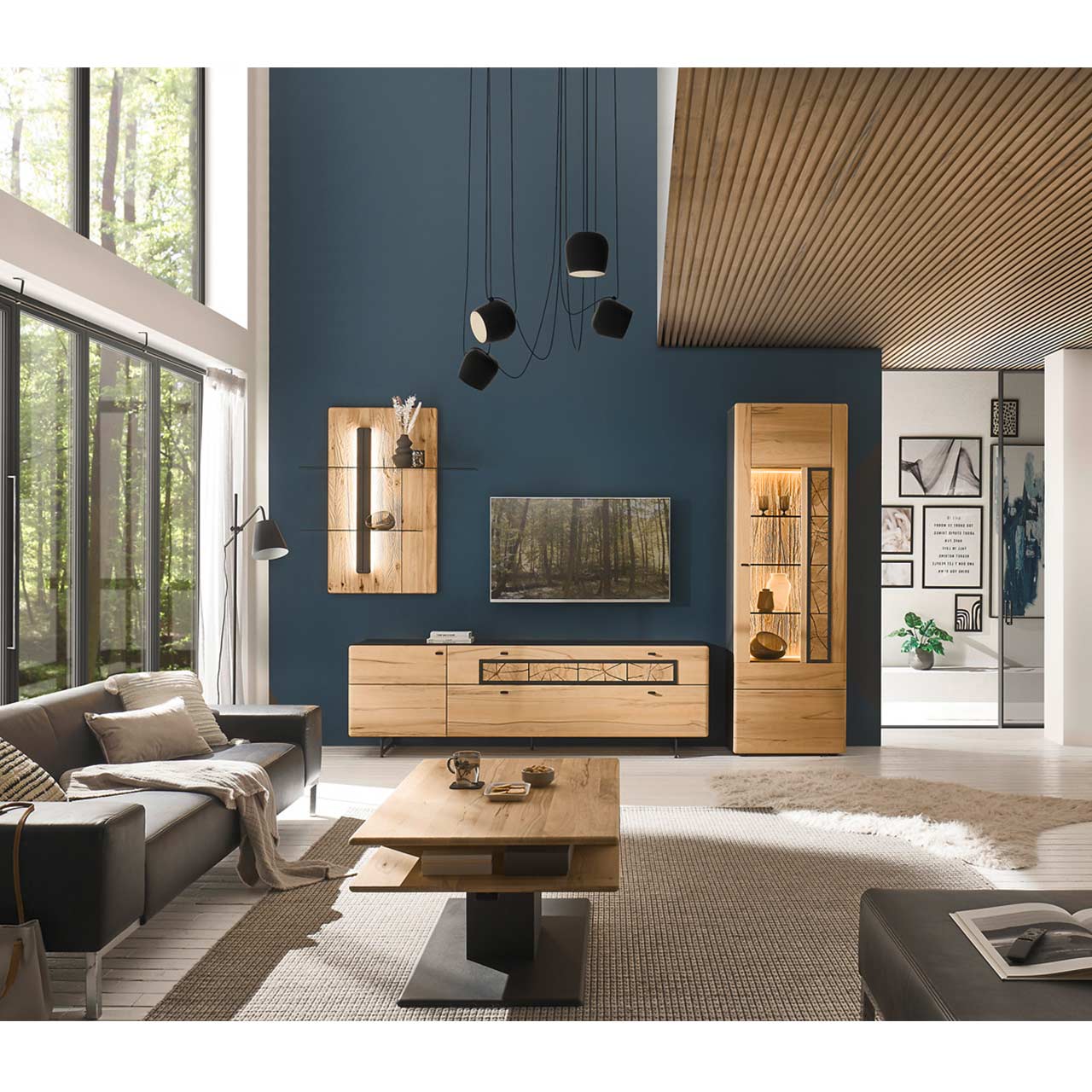 Modernes Wohnzimmers mit Fernseher, grauer Couch und einer Massivholzwohnwand aus Kernbuche vor einer dunkelblauen Wand bestehend aus Hochvitrine, Lowboard und Wandpaneel mit Glasablage. Im Vordergrund steht der passende rechteckige Couchtisch.