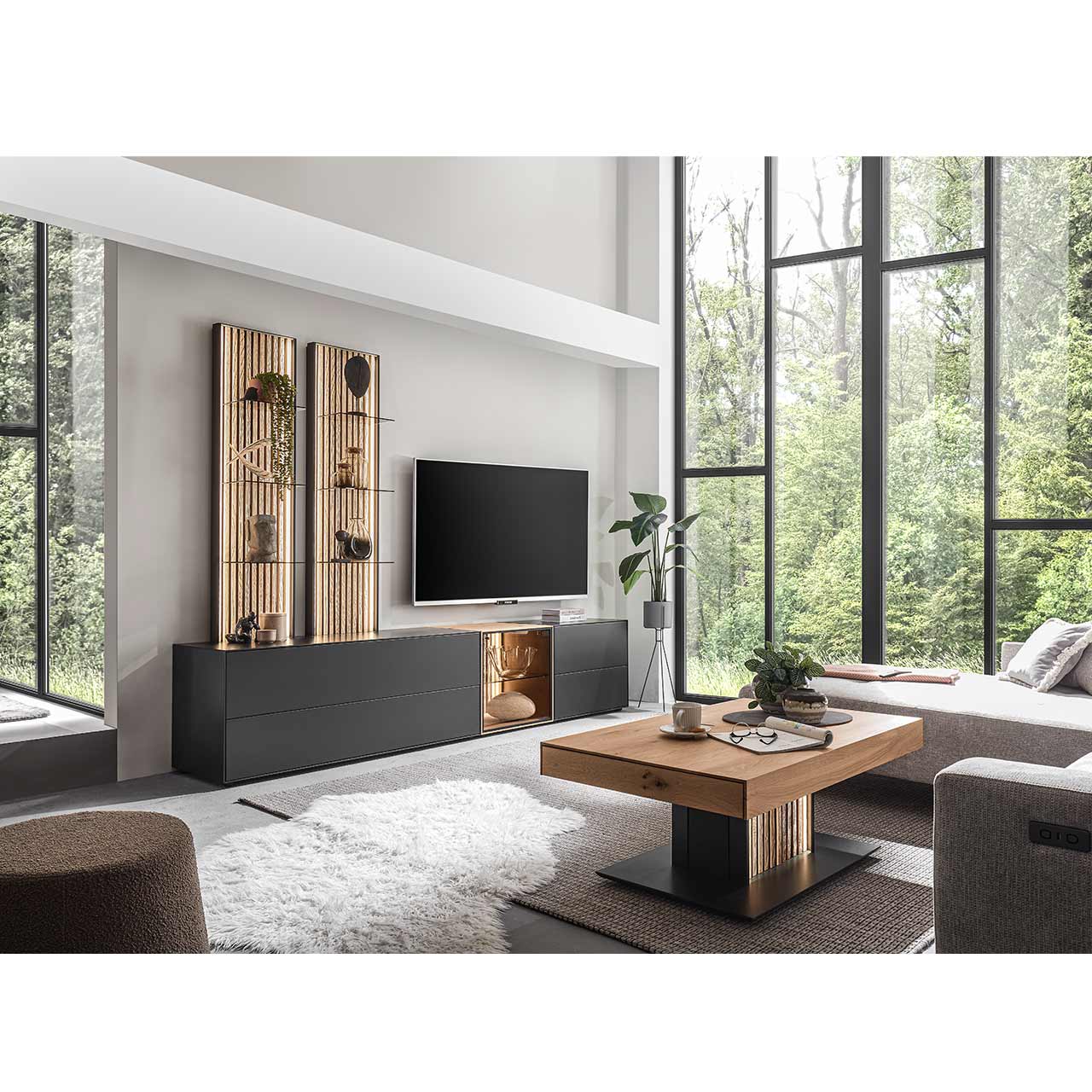 Modern eingerichtetes Wohnzimmer mit fünfteiliger Wohnwand bestehend aus Lowborads in anthrazit mit Glastüren und Wandpaneelen in hellem Holz mit Lamellen. Davor der passende helle Couchtisch.