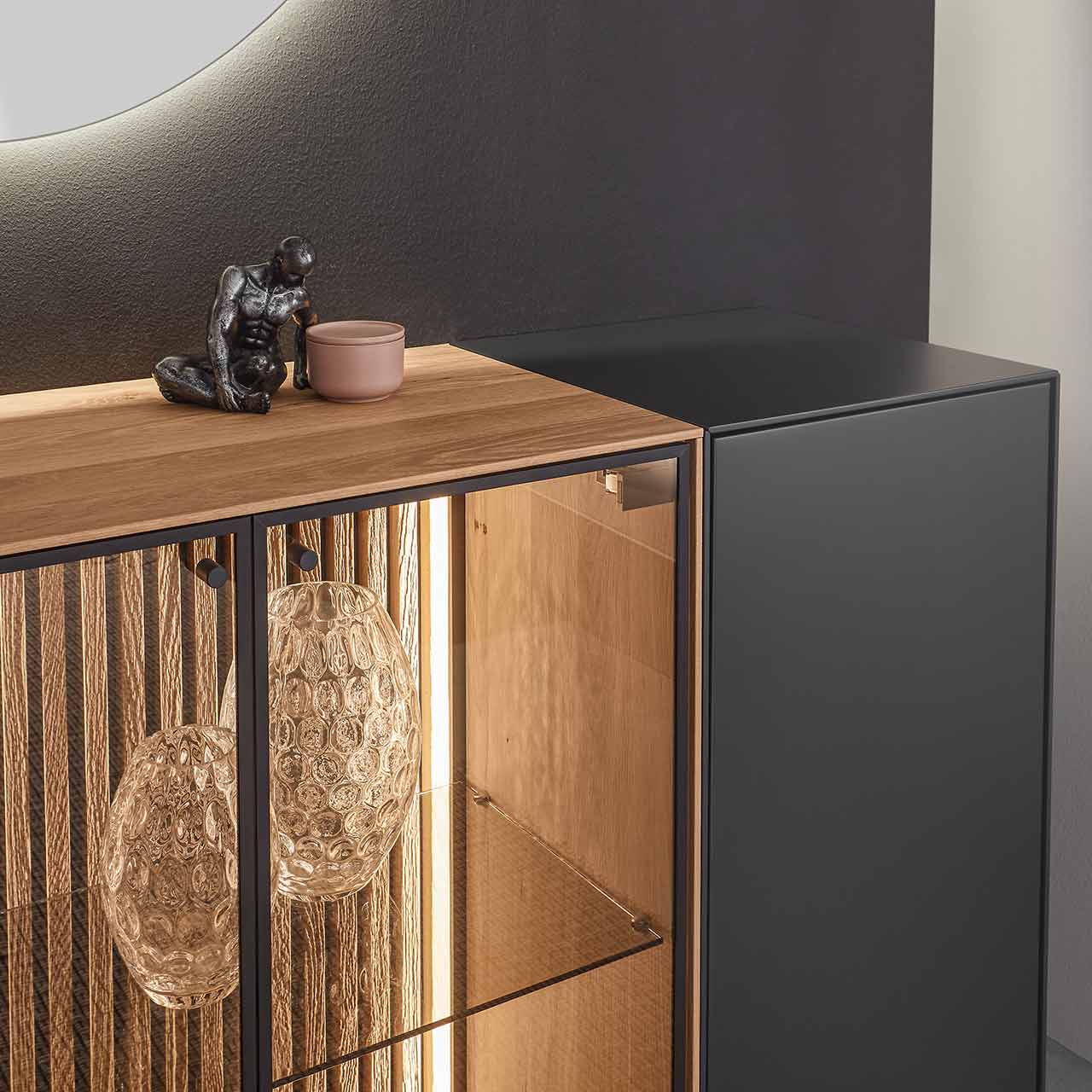 Detailaufnahme der Glastür aus Parsolbronze mit beleuchteter Lamellenrückwand von einem Sideboard aus massiver Birke anthrazit lackiert.