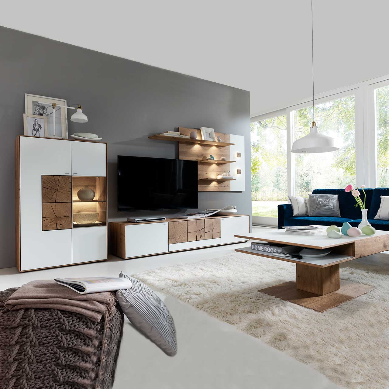 Wohnzimmer mit moderner dreiteiliger Massivholz Wohnwand mit Mattglas weiß Fronten und dekorativen Hirnholzscheiben: Langes Lowboard mit Hirnholz und Kufen, Wandpaneel mit Regalböden, Highboard mit beleuchtetem Glasausschnitt und Hirnholz.