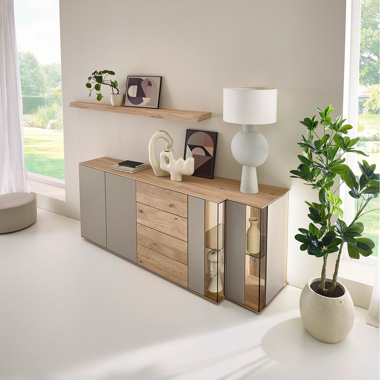 Moderne Kommode aus massiver Kerneiche mit Lackfronten Sand und Riffholz. Mit Lacktüren, Schubkasten und Tür mit Riffholzfront sowie zwei Glas-Lacktüren in asymmetrischem Design und beleuchteter Riffholzrückwand. Darüber Riffholz-Wandboard.