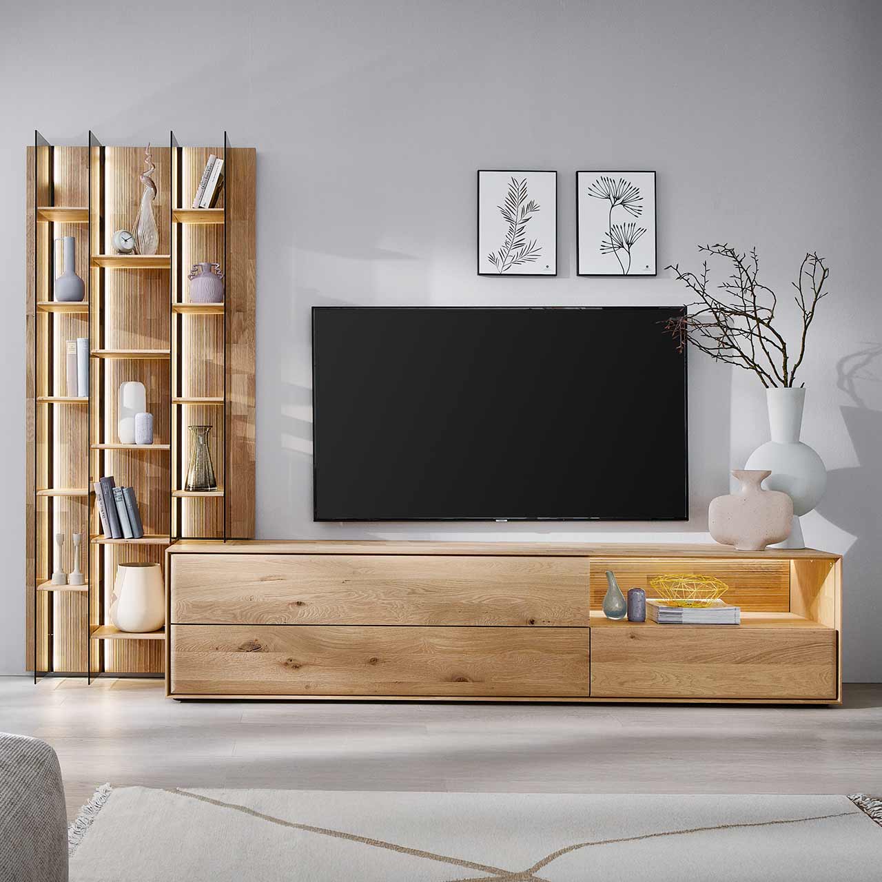 Hartmann VALA - Wohnkombination 8640 Nr. V38 - zweiteilig Moderne zweiteilige Wohnwand aus massiver Kerneiche Natur bestehend aus einem hohen Wandregal mit Holzböden, beleuchteten Glasseiten und geschroppter Rückwand und einem darin integriertem Lowboard mit beleuchteter Nische und Schubkasten.