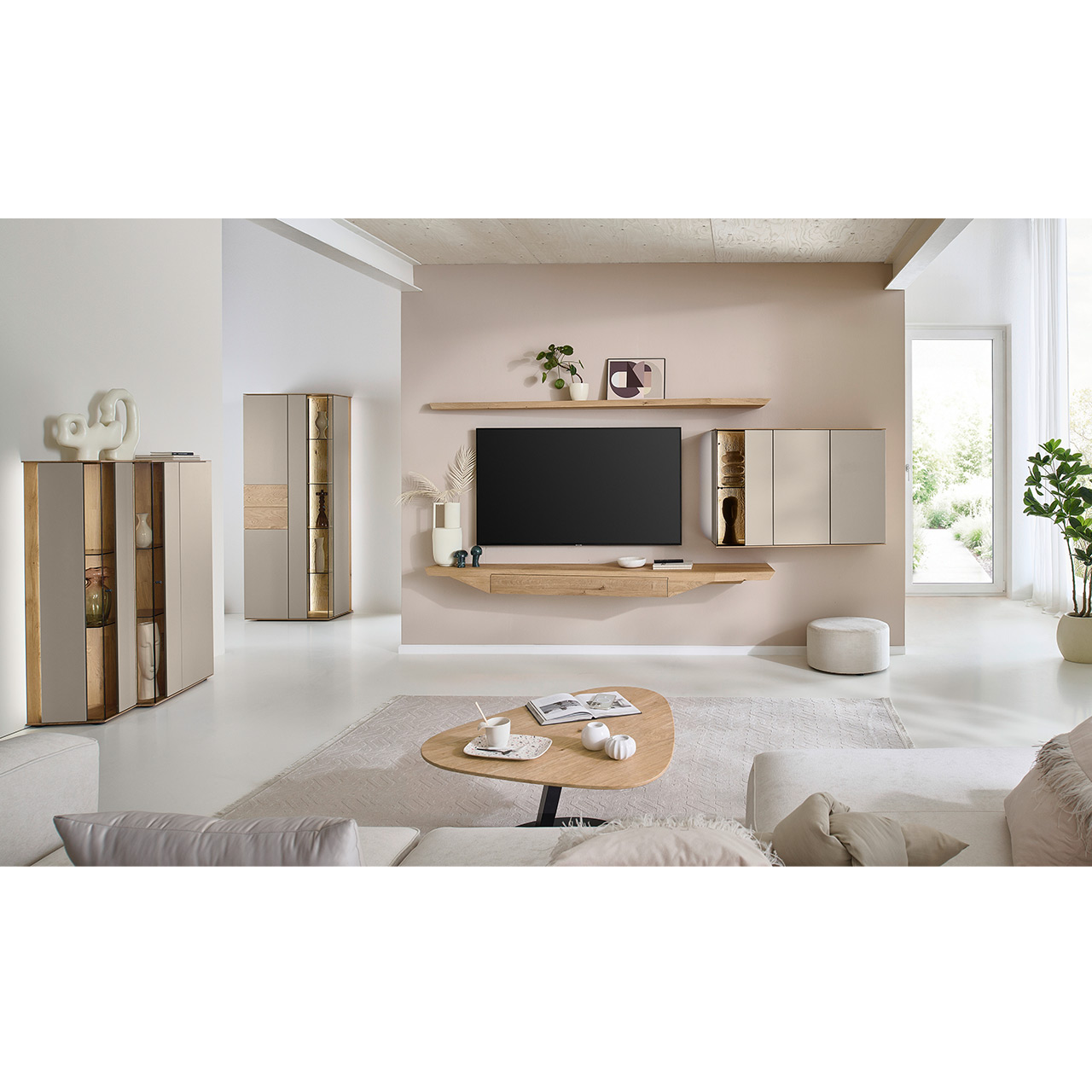 Hartmann Möbel SVEA - Wohnwand 8660 Nr. V28 SV - dreiteilig aus Kerneiche Natur, Lack Sand - Milieubild Wohnzimmer mit moderner Massivholzwohnwand mit Lack Sand bestehend aus Hängelowboard, Hängevitrine und Wandboard - im asymmetrischen Design. Links passendes Highboard mit Glastüren, davor asymmetrischer Beistelltische aus Holz.