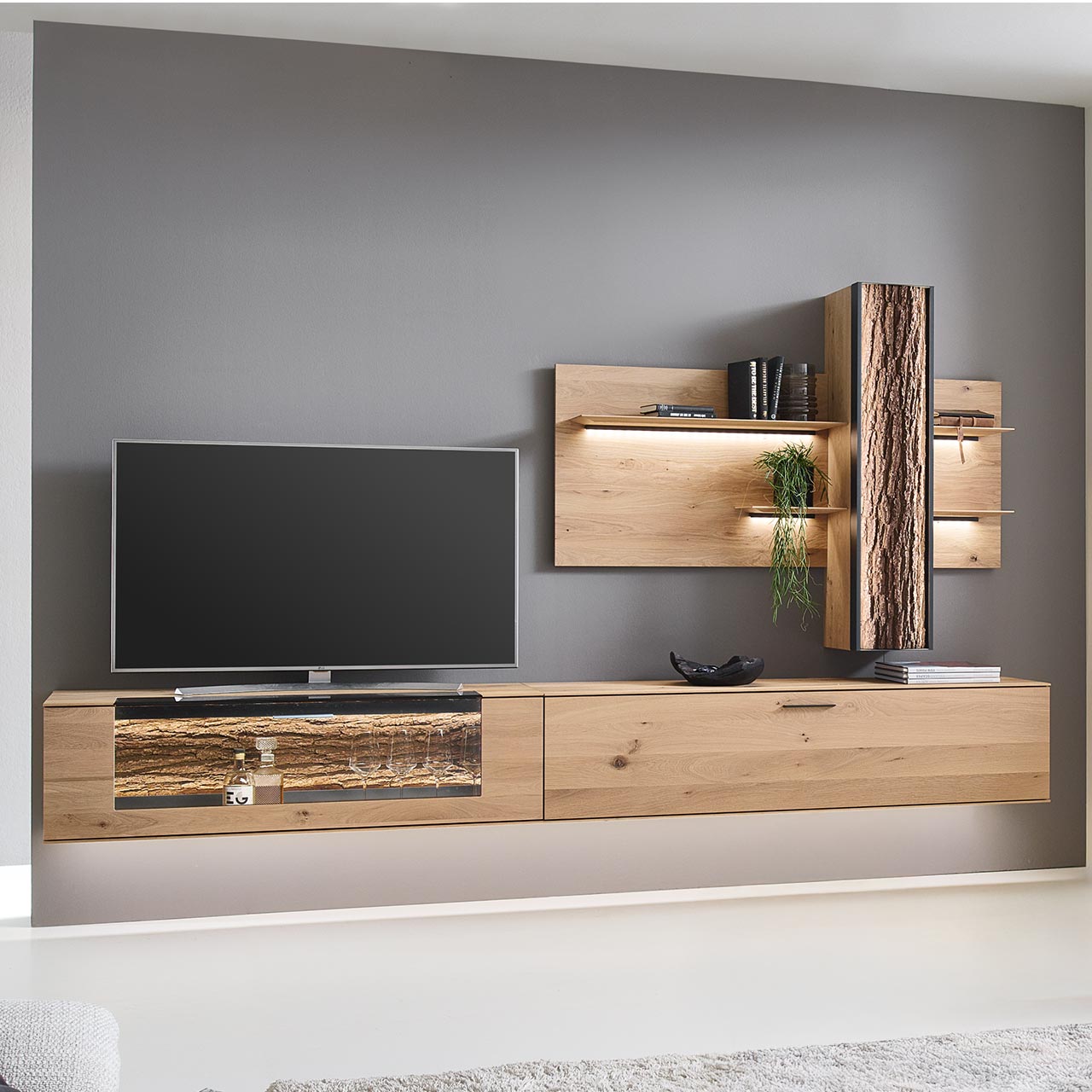 Moderne dreiteilige Wohnwand bestehend aus zwei Hängelowboards aus massiver Kerneiche Natur, eines mit beleuchtetem Glasausschnitt und Rinden-Akzent, und einem Wandpaneel mit vier beleuchteten Holzböden sowie integriertem Stauraumschrank. 