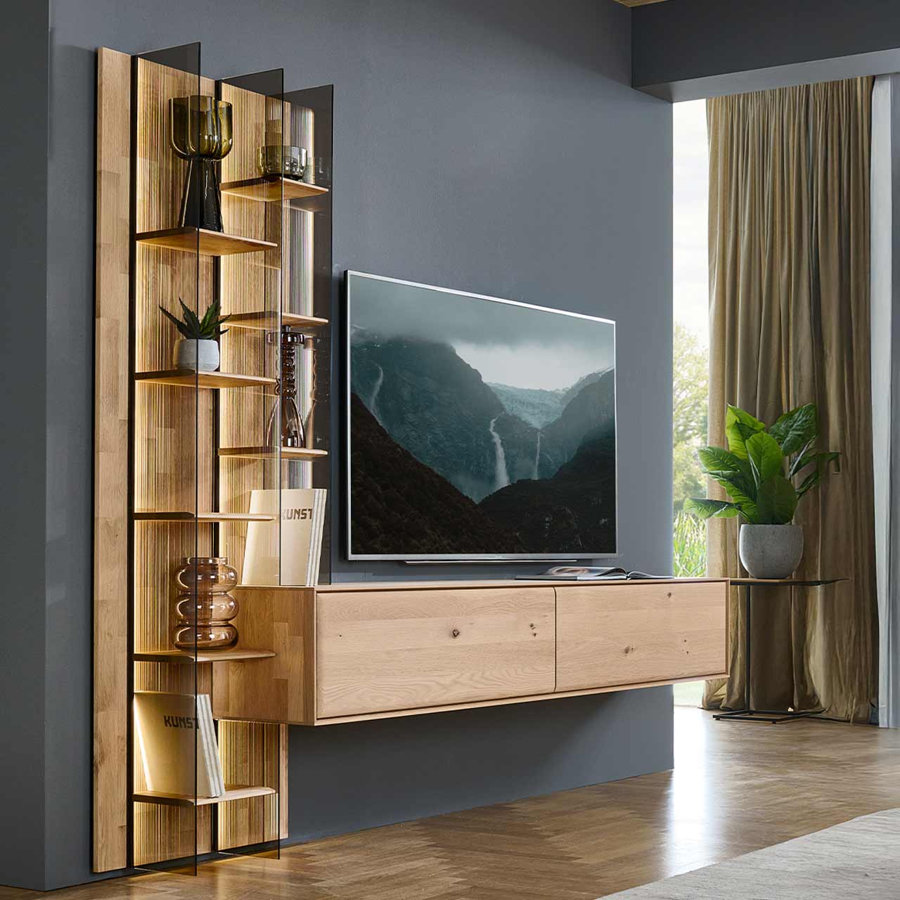 Moderne zweiteilige Wohnwand aus massiver Kerneiche Natur bestehend aus einem hohen Wandregal mit Holzböden, beleuchteten Glasseiten und geschroppter Rückwand und einem darin integriertem Hängelowboard.
