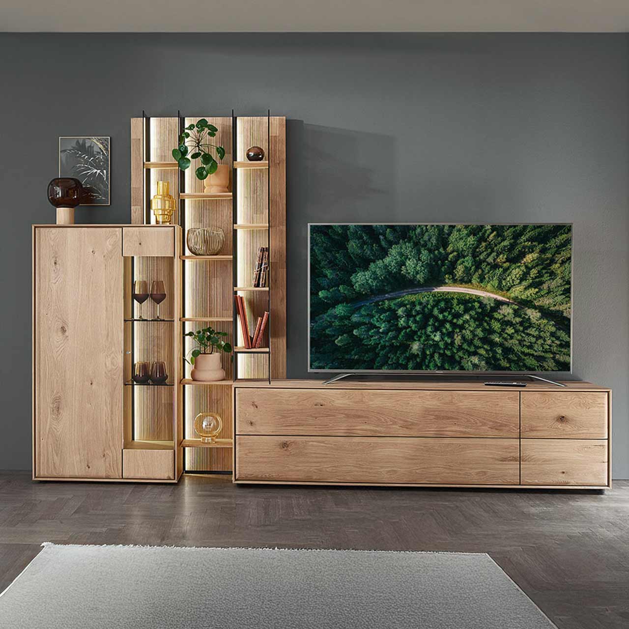 Moderne dreiteilige Wohnwand aus massiver Kerneiche Natur bestehend aus einem Highboard mit Glastür, einem hohen Wandregal mit Holzböden, beleuchteten Glasseiten und geschroppter Rückwand und einem darin integriertem Lowboard.