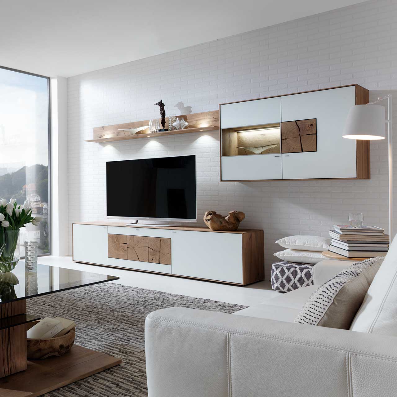 Wohnzimmer mit TV und moderner dreiteiliger Massivholz Wohnwand aus Kerneiche Umato mit Mattglas weiß Fronten: Langes Lowboard mit dekorativem Hirnholz, Wandregal aus Holz, Hängevitrine mit beleuchtetem Glasausschnitt und Hirnholz.