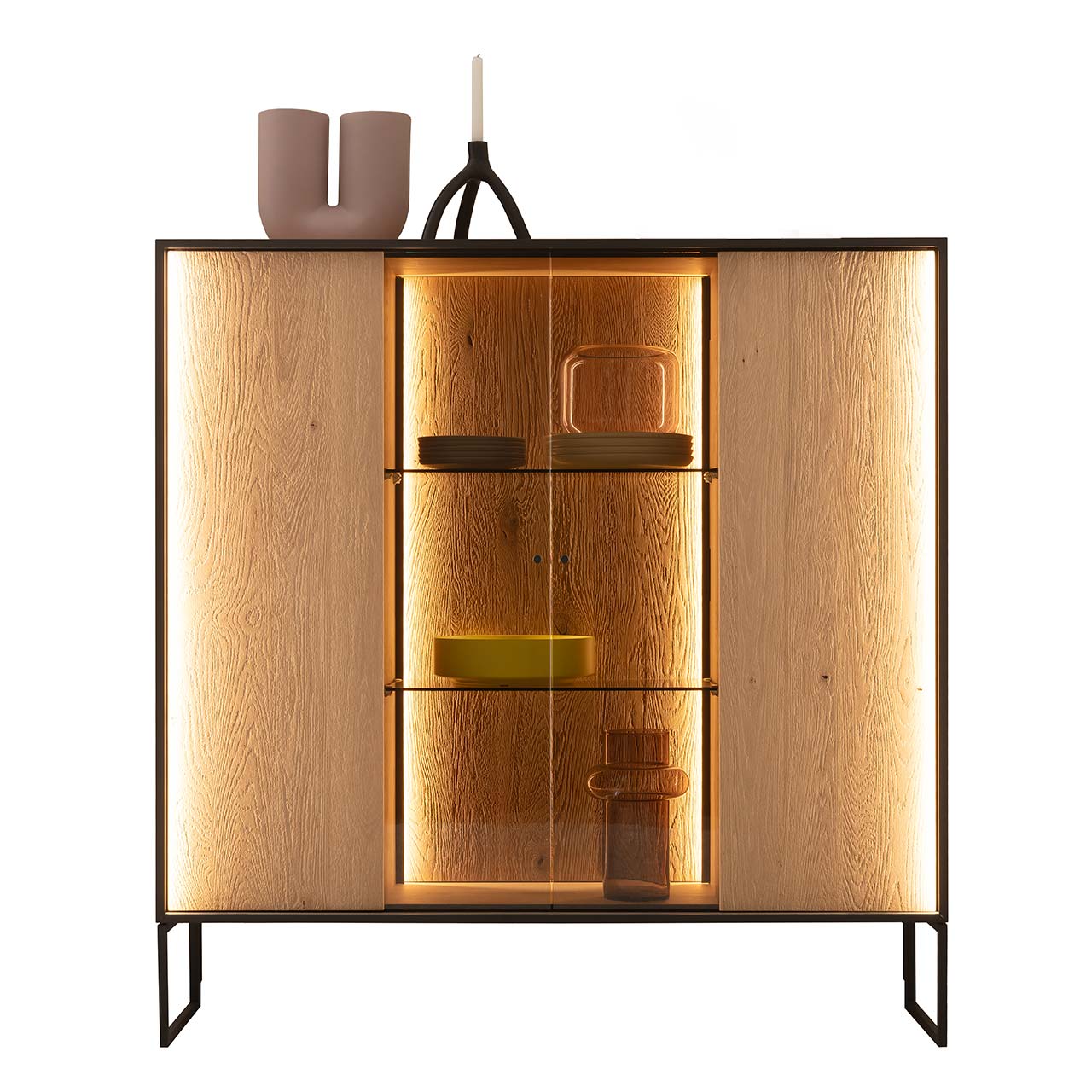 Hartmann YOLA Schöner Wohnen - Highboard mit hohen Kufen 8590-6134 Modernes Highboard aus massiver, sandgestrahlter Kerneiche Natur mit beleuchtetem, rundum Metallrahmen und zwei filigranen Metallfüßen in Anthrazit. Mit zwei Holztüren links und rechts, mittig verglaster Vitrinenbereich mit beleuchteten Glaseinlegeböden.