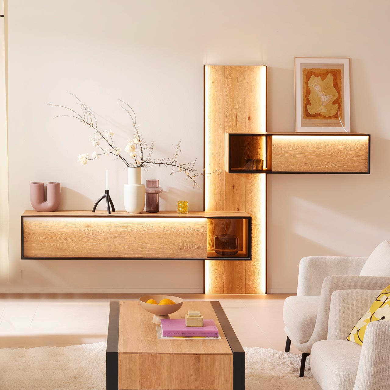 Minimalistische Wohnwand aus massiver, sandgestrahlter Kerneiche Natur mit anthrazitfarbenem Metallrahmen, bestehend aus langem, beleuchtetem Wandpaneel, oben seitlich angebrachtem Hängeregal mit Glasausschnitt und Lowboard mit Glasdetail unten.