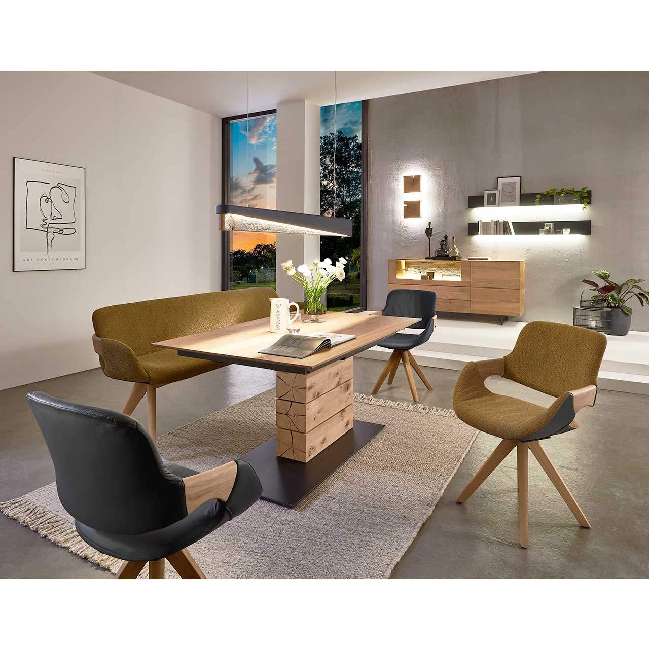 Milieubild Esszimmer - Hartmann NATURZEIT 7100E/8400E - 1552 Esstisch T100 Modernes Esszimmer mit massivem, rechteckigem Holztisch, umgeben von drei Stühlen auf Holzgestell und passender Sitzbank in Senffarbe. Über dem Tisch hängt eine Holz-Balkenleuchte. Rechts an der Wand das passende Sideboard und zwei Metallregale.