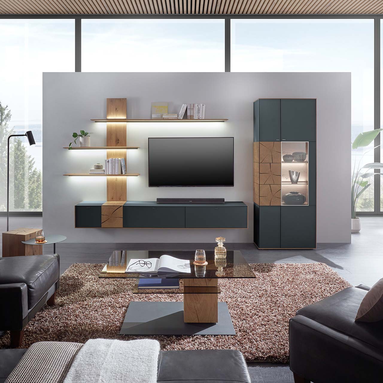 Wohnzimmer mit TV und moderner Wohnwand aus massiver Kerneiche mit Mattglas anthrazit Fronten, mit Hängelowboard, Wandpaneel mit Regalböden und Standvitrine. Im Vordergrund der passende Couchtisch mit rechteckiger Glasplatte.