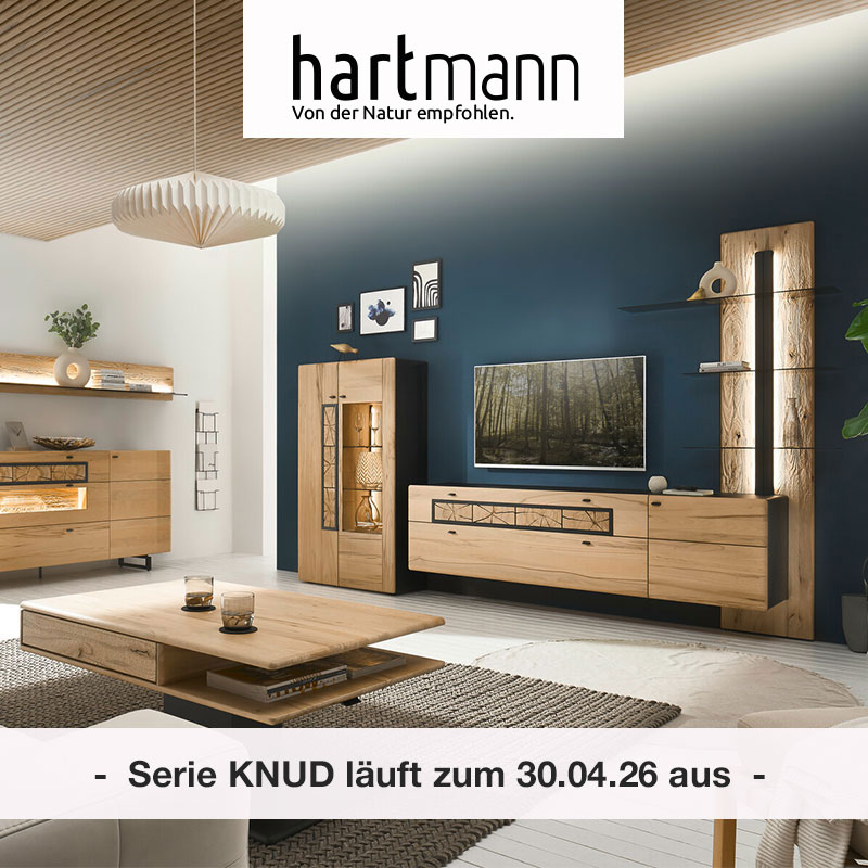 Hartmann KNUD - Massivholzmöbel aus heller Kernesche kombiniert mit anthrazit & dekorativen Hirnholzscheiben. Möbelprogramm läuft zum 3 30.04.26. Ambientebild zeigt Lowboard mit Hirnholz, beleuchtetes Wandpaneel mit Glasböden & Highboard mit Glastür.