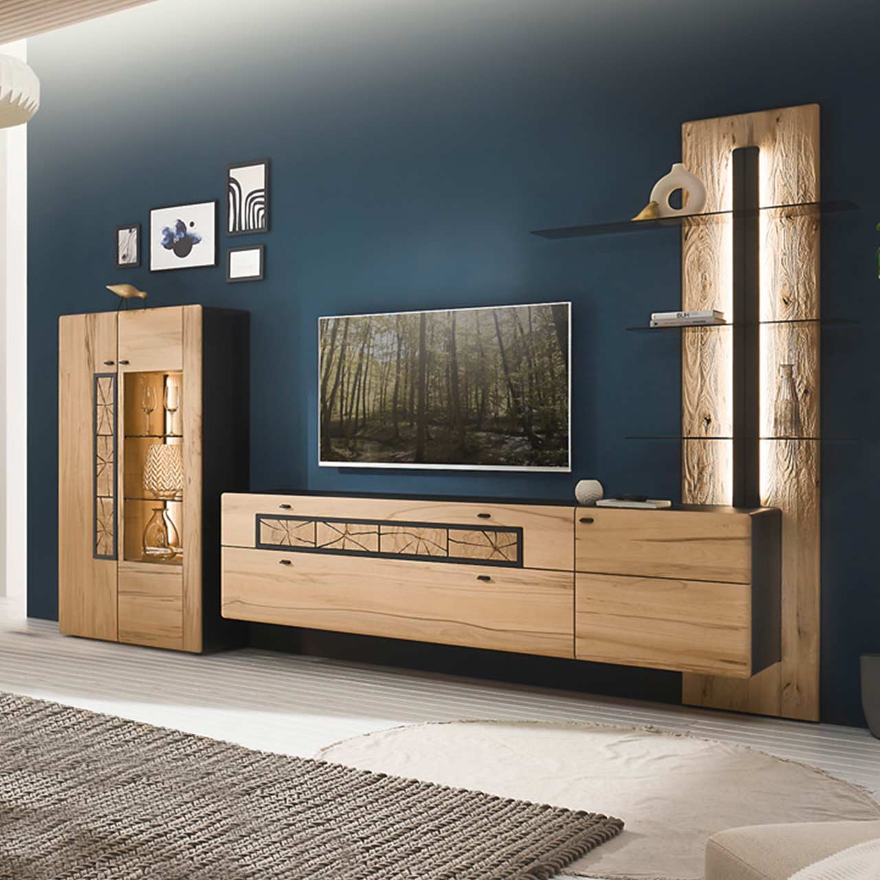 Wohnzimmer - Möbel-Serie Hartmann KNUD 5580 - Wohnwand Nr. 20 Modernes Wohnzimmer mit dreiteiliger Massivholzwohnwand aus heller Kernbuche vor dunkelblauer Wand: Highboard mit Glasfront, Hängelowboard mit Schubkästen, Wandpaneel mit anthrazitfarbener vertikaler Profilleiste und drei Glasböden.
