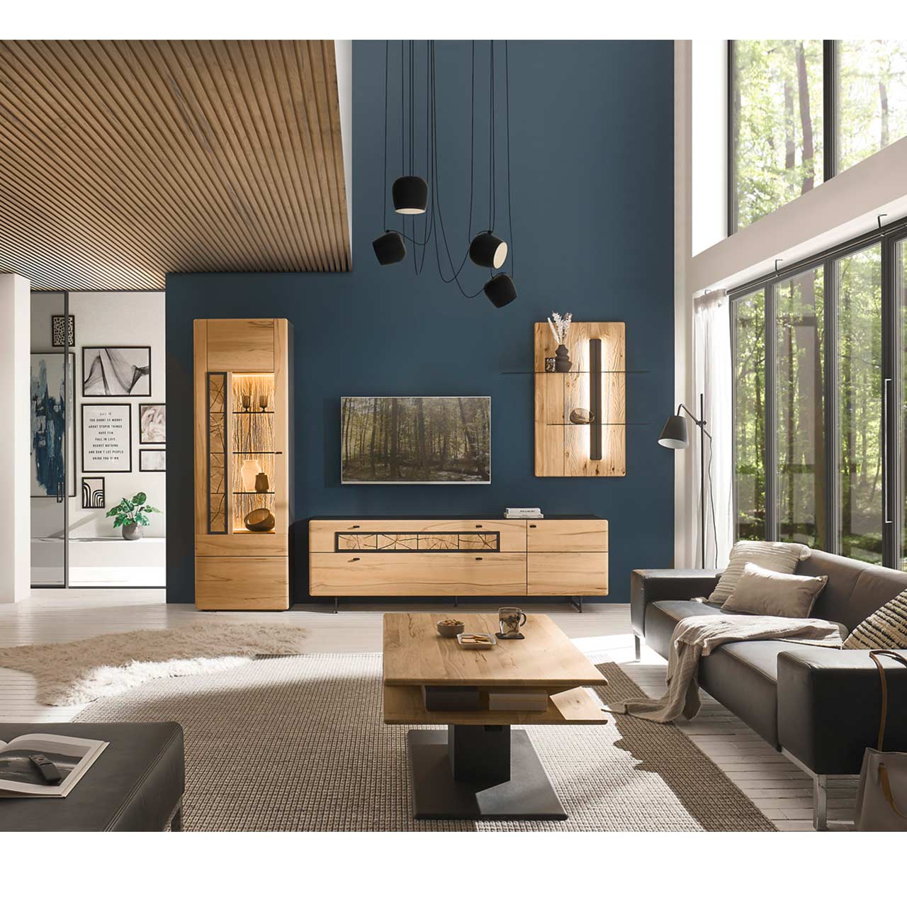 Modernes Wohnzimmers mit Fernseher, grauer Couch und einer Massivholzwohnwand aus Kernbuche vor einer dunkelblauen Wand bestehend aus Hochvitrine, Lowboard und Wandpaneel mit Glasablage. Im Vordergrund steht der passende rechteckige Couchtisch.