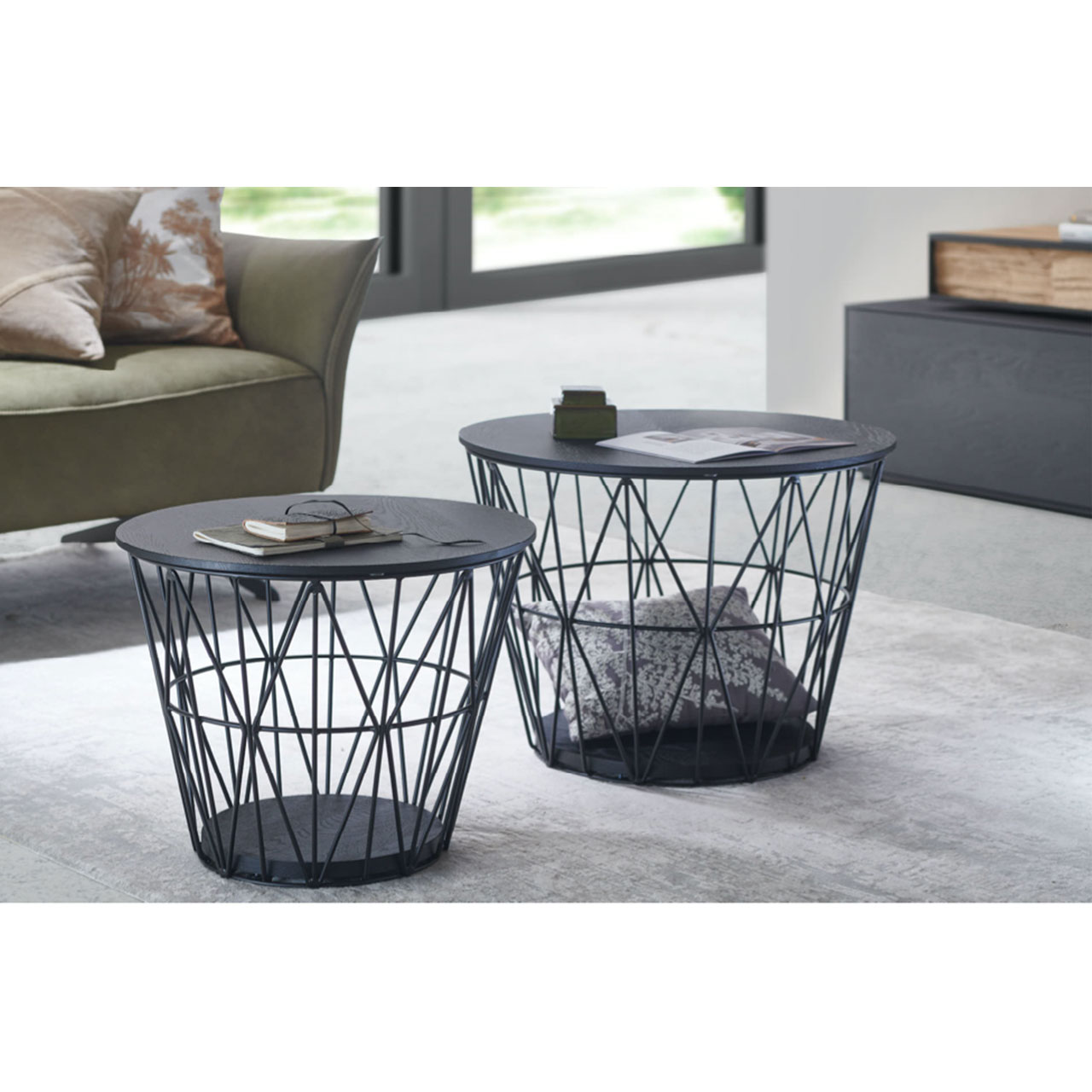Zwei raffinierte, runde Beistelltische mit feinem Metallkorb in Anthrazit und abnehmbarem Holzdeckel sowie Bodenplatte aus Kernesche anthrazit – im Wohnzimmer stehend.