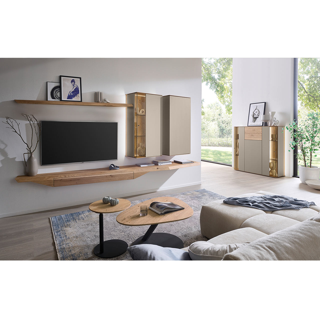 Wohnzimmer mit moderner Massivholzwohnwand bestehend aus Hängelowboard mit Schubkasten, Hängevitrine, Hängeschrank sowie Wandboard - im asymmetrischen Design. Rechts passendes Highboard mit Glastüren, davor zwei Beistelltische aus Holz.