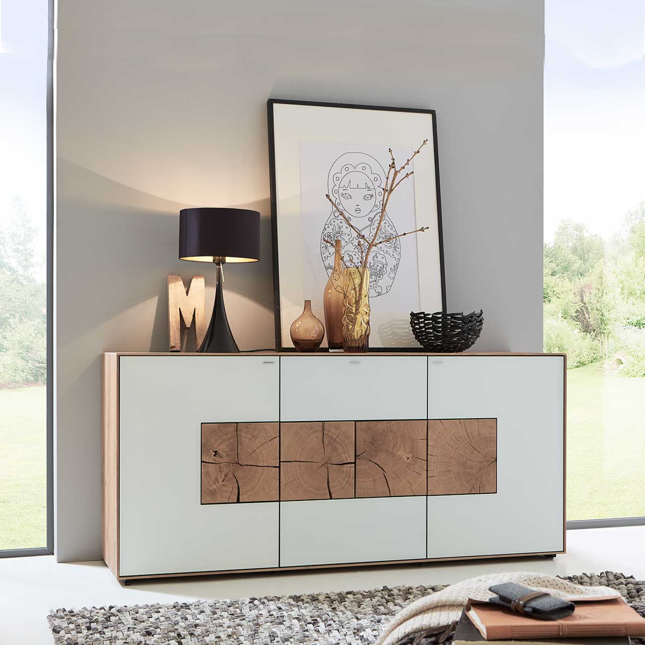 Flur mit modernem Sideboard aus massiver Kerneiche Umato mit weißfarbenen Mattglasfronten und vier dekorativen, rechteckigen Hirnholzscheiben - vor hellgrauer Wand.