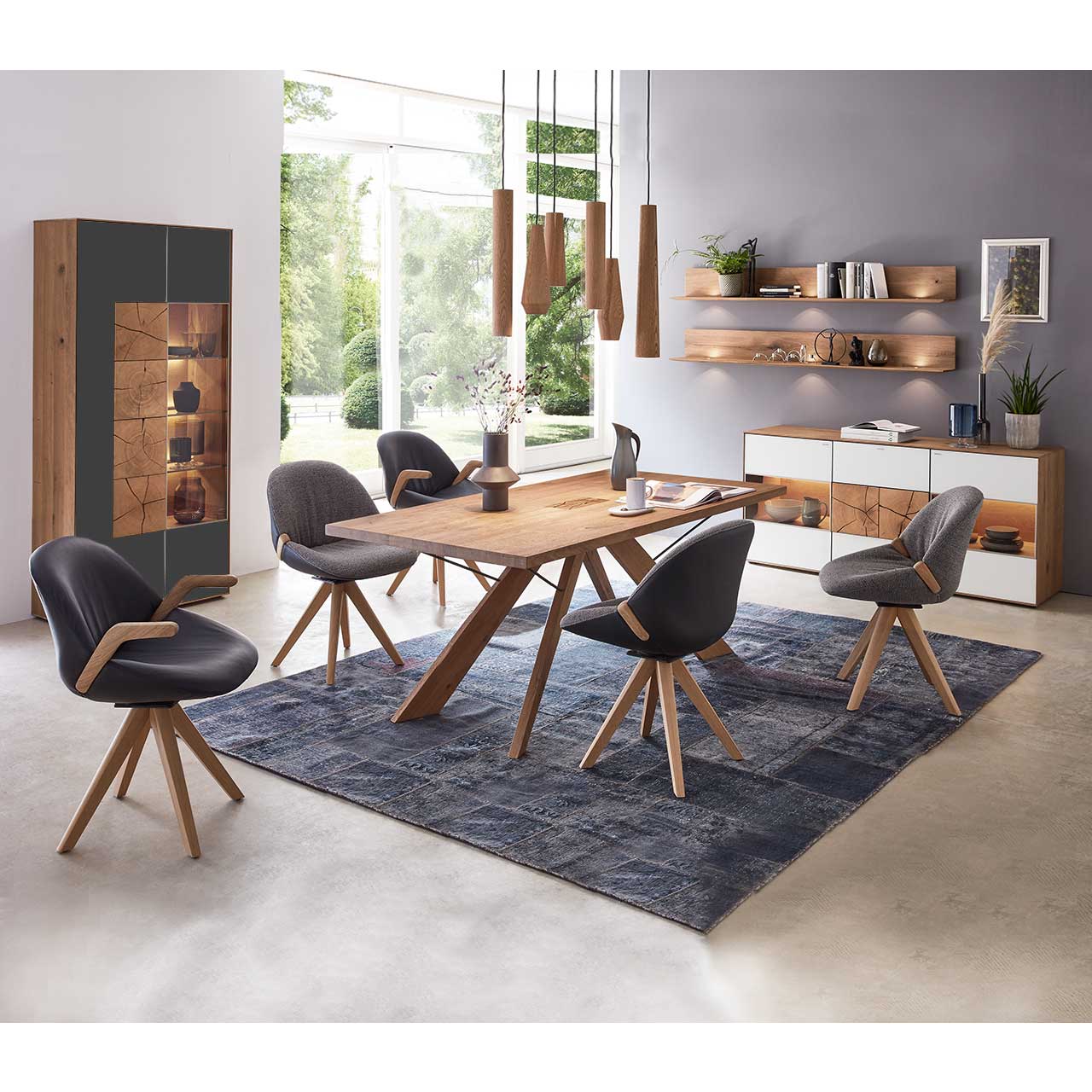 passende Sideboard und zwei Wandregale. Milieubild Esszimmer - Hartmann CAYA - Standvitrine 7170-0092A li. Esszimmer mit massivem Holztisch und fünf Stühlen mit Holzgestell, links an der Wand stehend eine Strandvitrine in Mattglas anthrazit und beleuchtetem Glasausschnitt mit drei Glasböden. Rechts das passende Sideboard und zwei Wandregale.