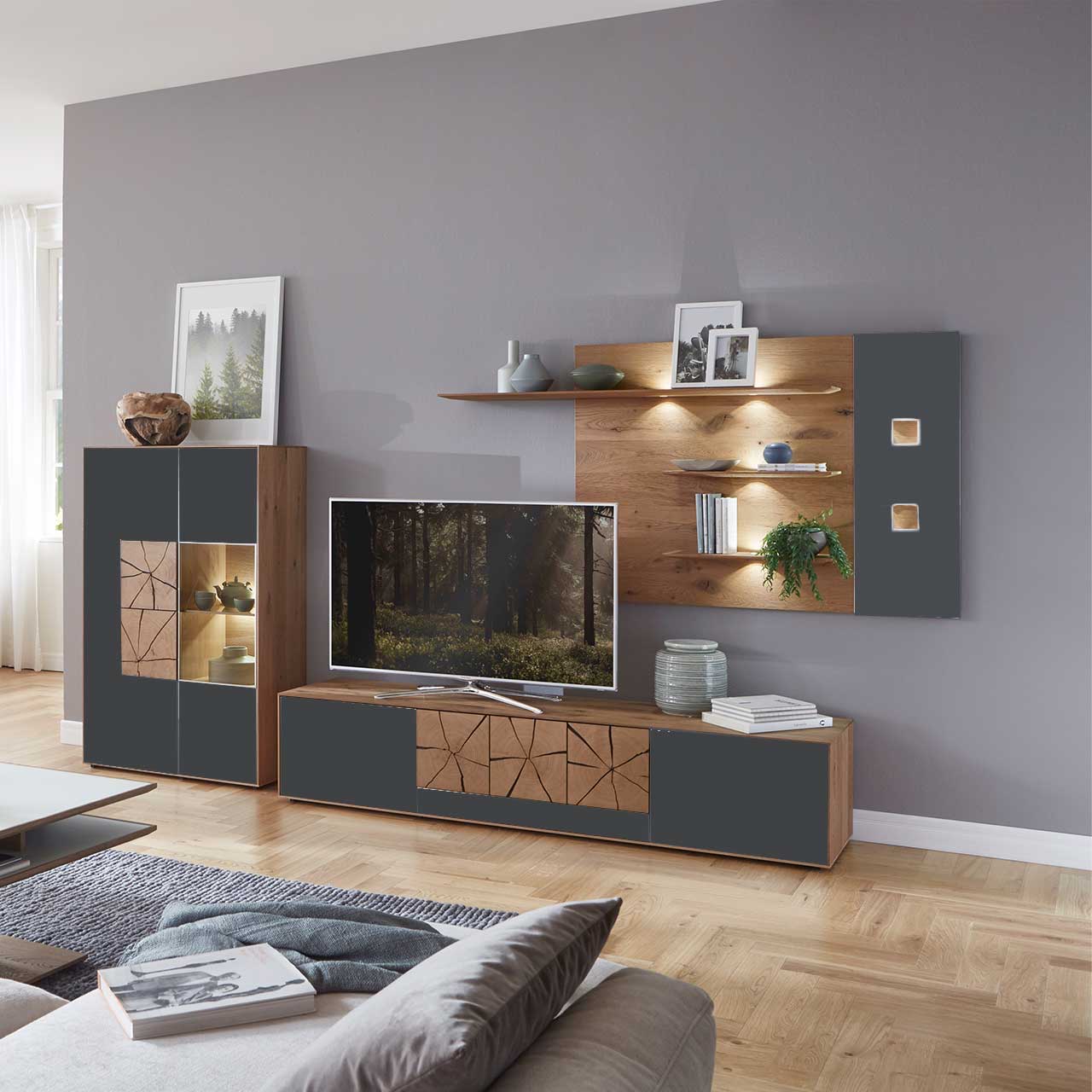 Wohnzimmer mit moderner dreiteiliger Massivholz Wohnwand mit Mattglas Anthrazit Fronten und dekorativen Hirnholzscheiben: Langes Lowboard mit Hirnholz und Kufen, Wandpaneel mit Regalböden, Highboard mit beleuchtetem Glasausschnitt und Hirnholz.