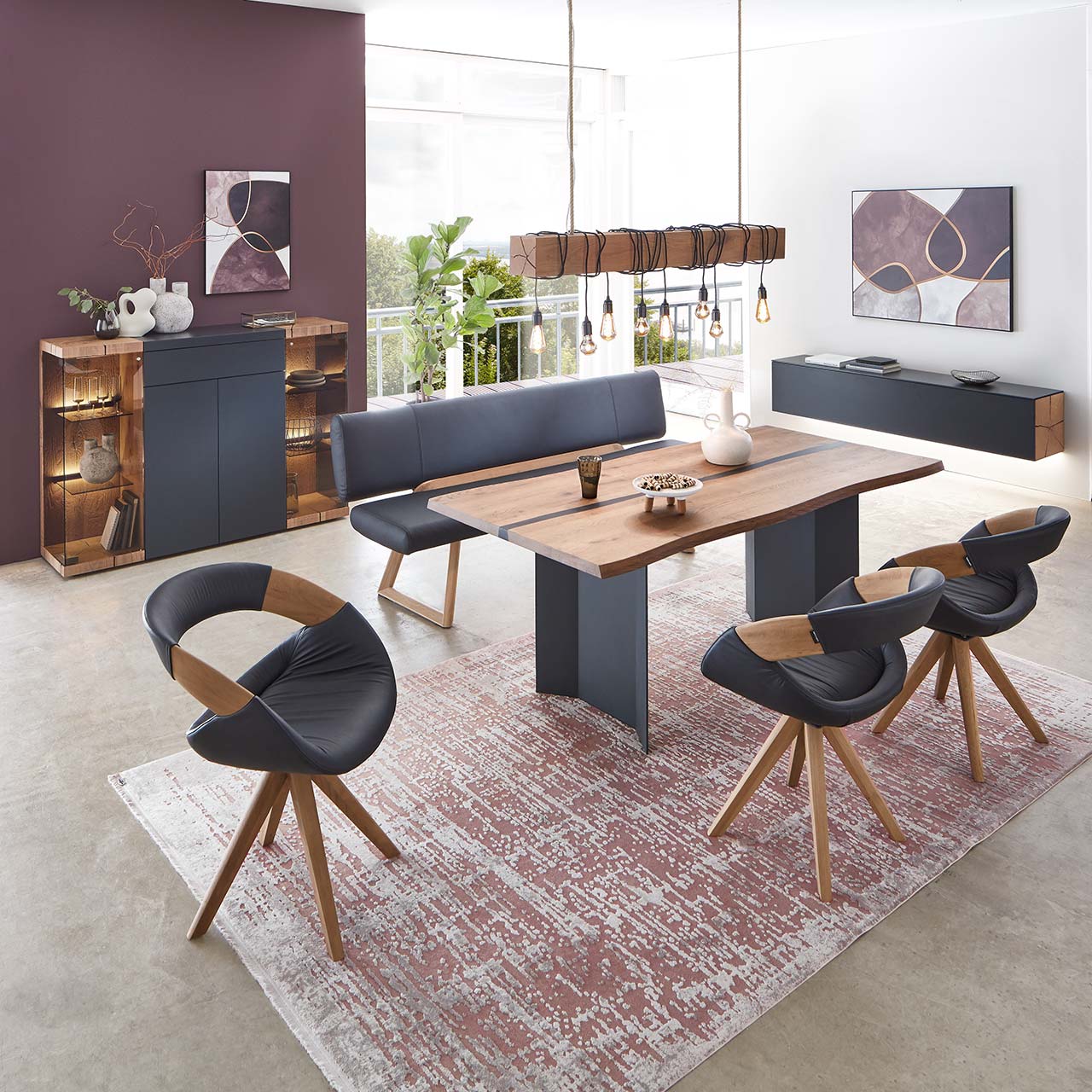 Modernes Esszimmer mit massivem, rechteckigen Holztisch, umgeben von drei Stühlen mit dunkelem Lederbezug auf Holzgestell und der passenden Polstersitzbank. Hinten an der Wand stehend die passenden Esszimmermöbel.