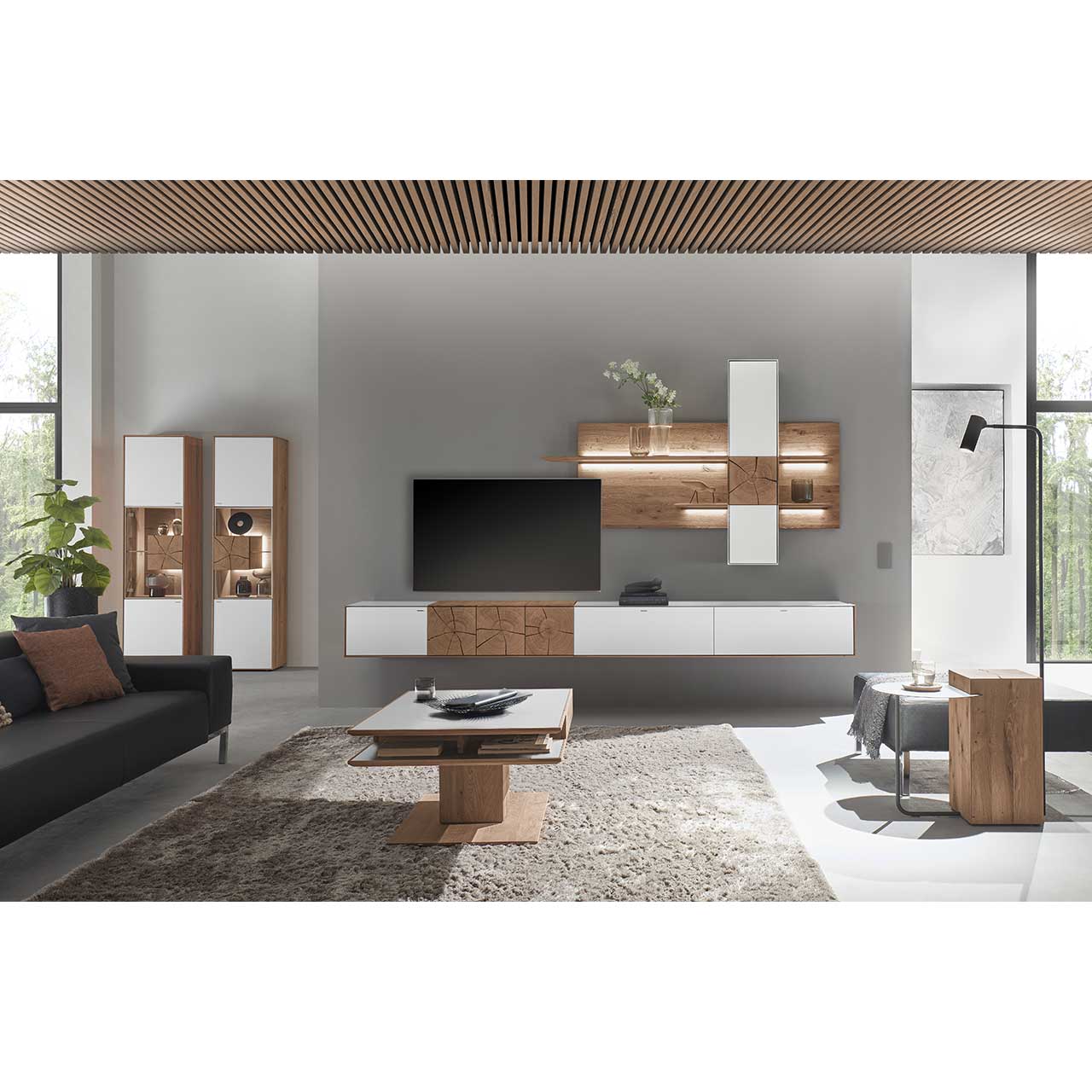 Wohnzimmer mit TV und moderner Wohnwand aus massiver Kerneiche mit Hirnholz und Mattglas weiß Fronten, mit Hängelowboard, Wandpaneel mit Regalböden und Hängeschrank. Hinten links zwei passende Standvitrinen. Im Vordergrund rechteckiger Couchtisch.