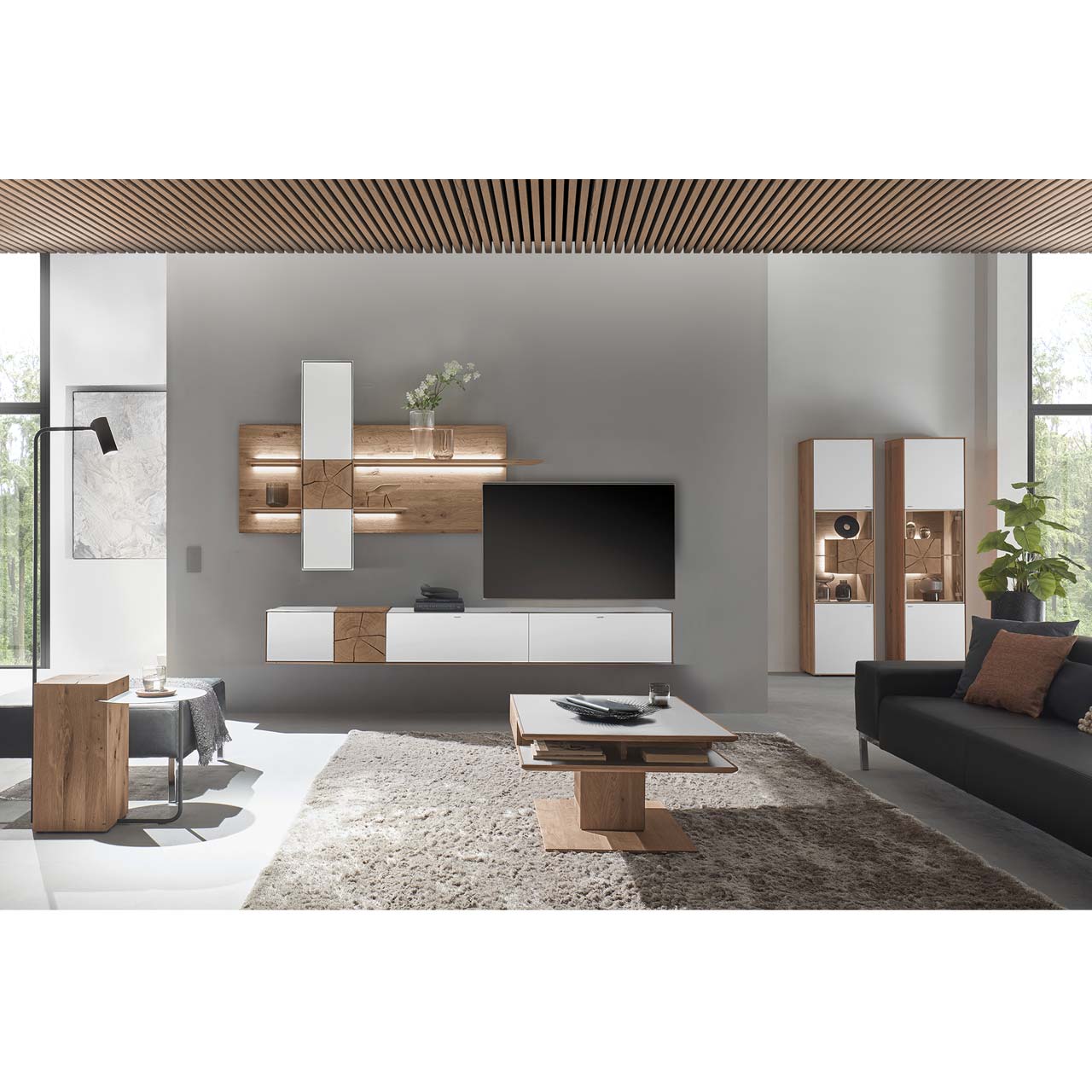 Wohnzimmer mit TV und moderner Wohnwand aus massiver Kerneiche mit Hirnholz und Mattglas weiß Fronten, mit Hängelowboard, Wandpaneel mit Regalböden und Hängeschrank. Hinten rechts zwei passende Standvitrinen. Im Vordergrund rechteckiger Couchtisch.