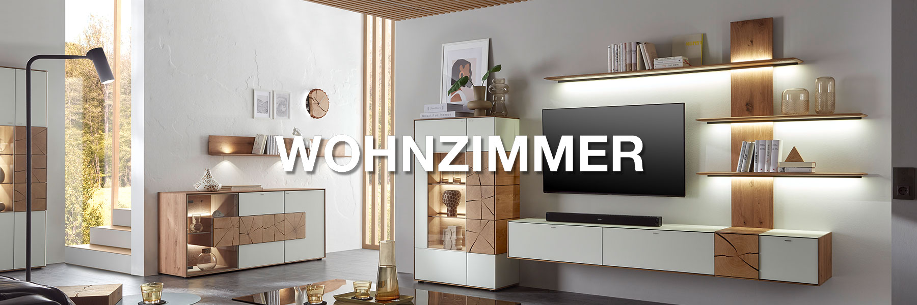 Wohnzimmermöbel der Marke Hartmann. Moderne Möbel wie Wohnwände, Highboards, Sideboards, Couchtische uvm. gefertigt aus massivem Holz und kombiniert mit Glas, Lack oder Metall. Ambientebild zeigt eine Massivholz Wohnwand der Serie CAYA in modernem Weiß.