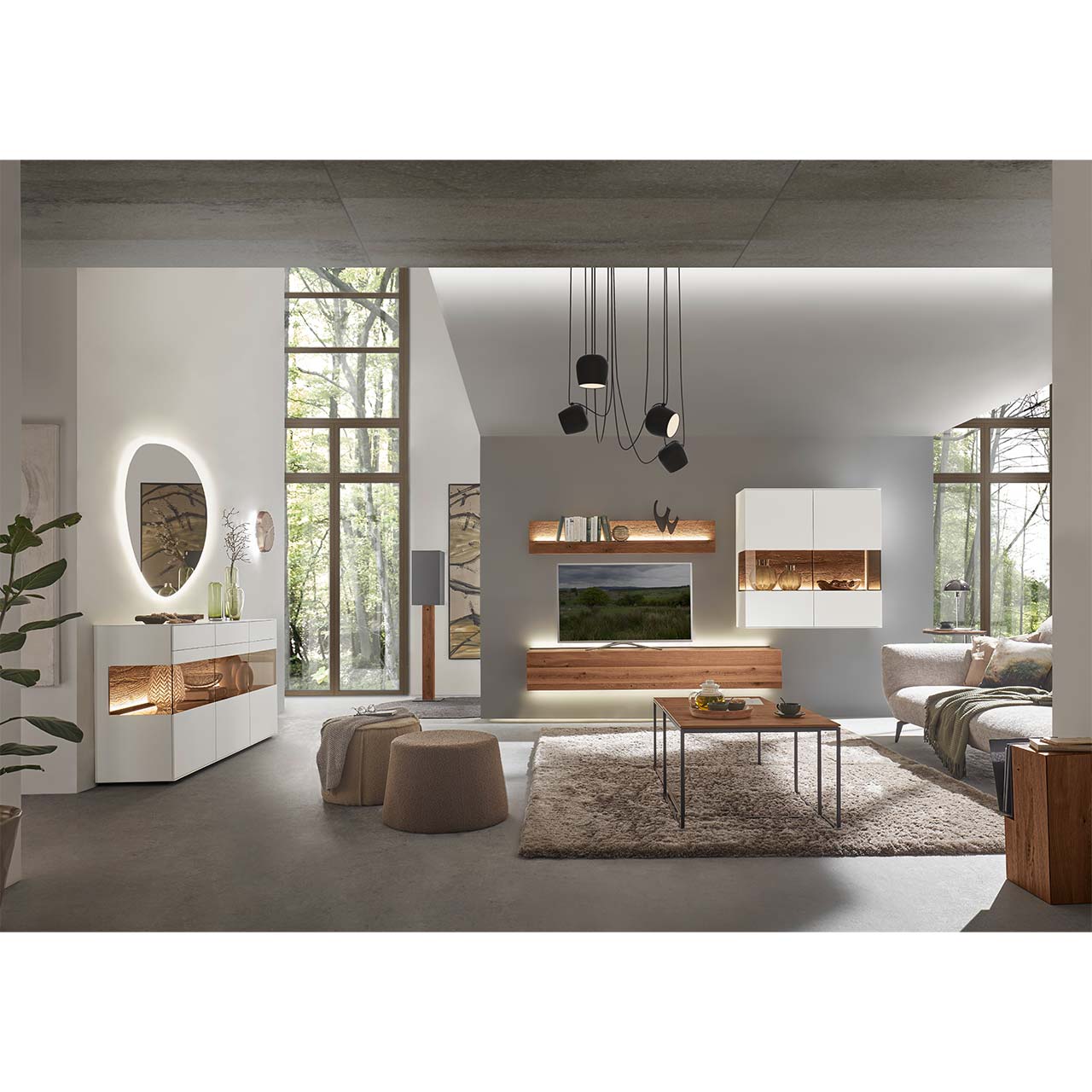 Modernes Wohnzimmer mit Wohnwand aus dunkler Kerneiche und Birke in Lack weiß: Hängelowboard, darüber Wandpaneel mit Glasablageboden, rechts weiße Hängevitrine. Links an der Wand weißes Highboard mit Glasausschnitt, davor rechteckiger Holz-Couchtisch.