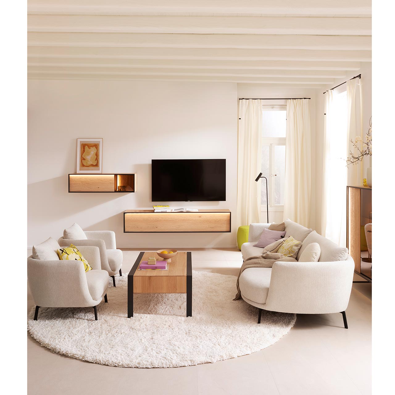 Modern eingerichtetes Wohnzimmer mit Massivholzmöbeln aus heller Kerneiche Natur: Schlichtes Hängelowboard und Hängeschrank mit Glasausschnitt, beide beleuchtet und eingefasst in Metallrahmen anthrazit. Davor Holz-Couchtisch auf Metallfüßen. 
