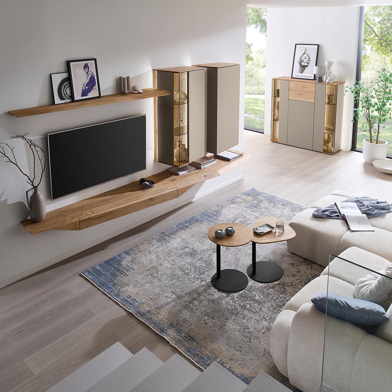 Hartmann Möbel SVEA - Wohnwand 8660 Nr. V26 SV - vierteilig aus Kerneiche Natur, Lack Sand - Milieubild Wohnzimmer mit moderner Massivholzwohnwand bestehend aus Hängelowboard, Hängevitrine, Hängeschrank sowie Wandboard - im asymmetrischen Design. Rechts passendes Highboard mit Glastüren, davor zwei Beistelltische aus Holz - Ansicht von oben.