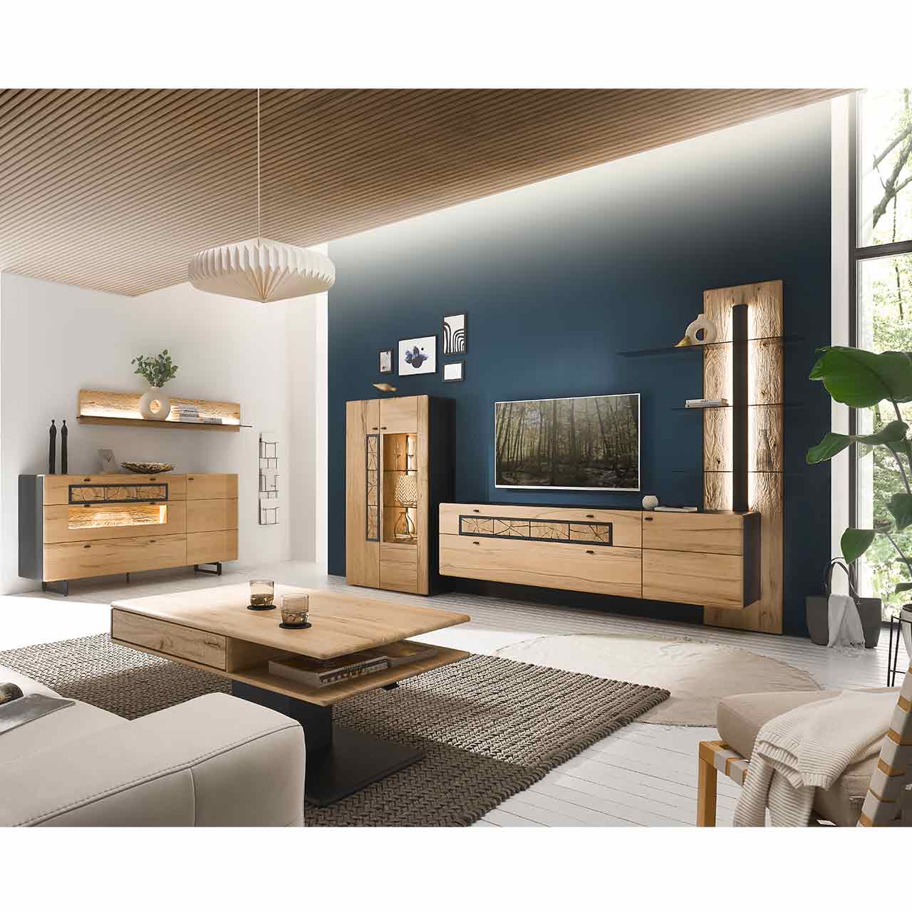 Modernes Wohnzimmer mit Möbeln aus heller Kernbuche: Sideboard auf Metallkufen mit Hirnholzscheiben und Glasfront, darüber Hängeregal. Rechts Highboard mit Holz-/Glastür, Hängelowboard und Wandpaneel mit drei Glasböden
