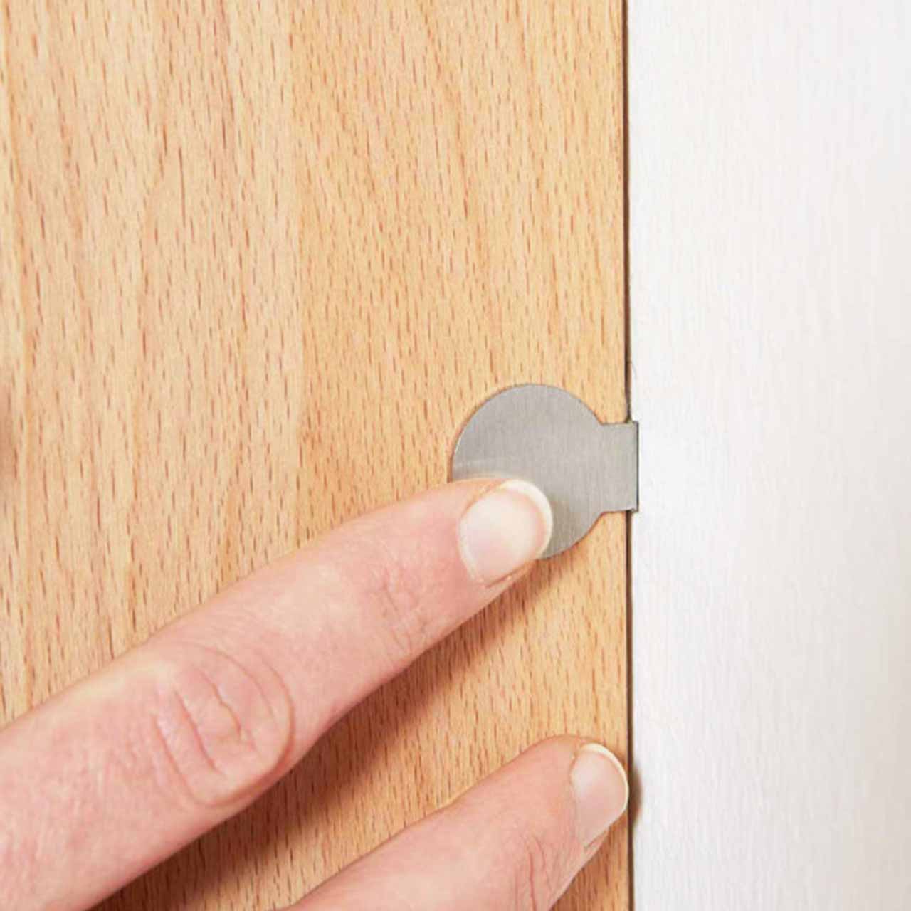 Hartmann SALVO Garderoben - Touchschalter 8550G-0140 Bildausschnitt eines runden, silbernen Touchschalters angebracht an einem Holzmöbelstück, der per Zeigefinger betätigt wird.