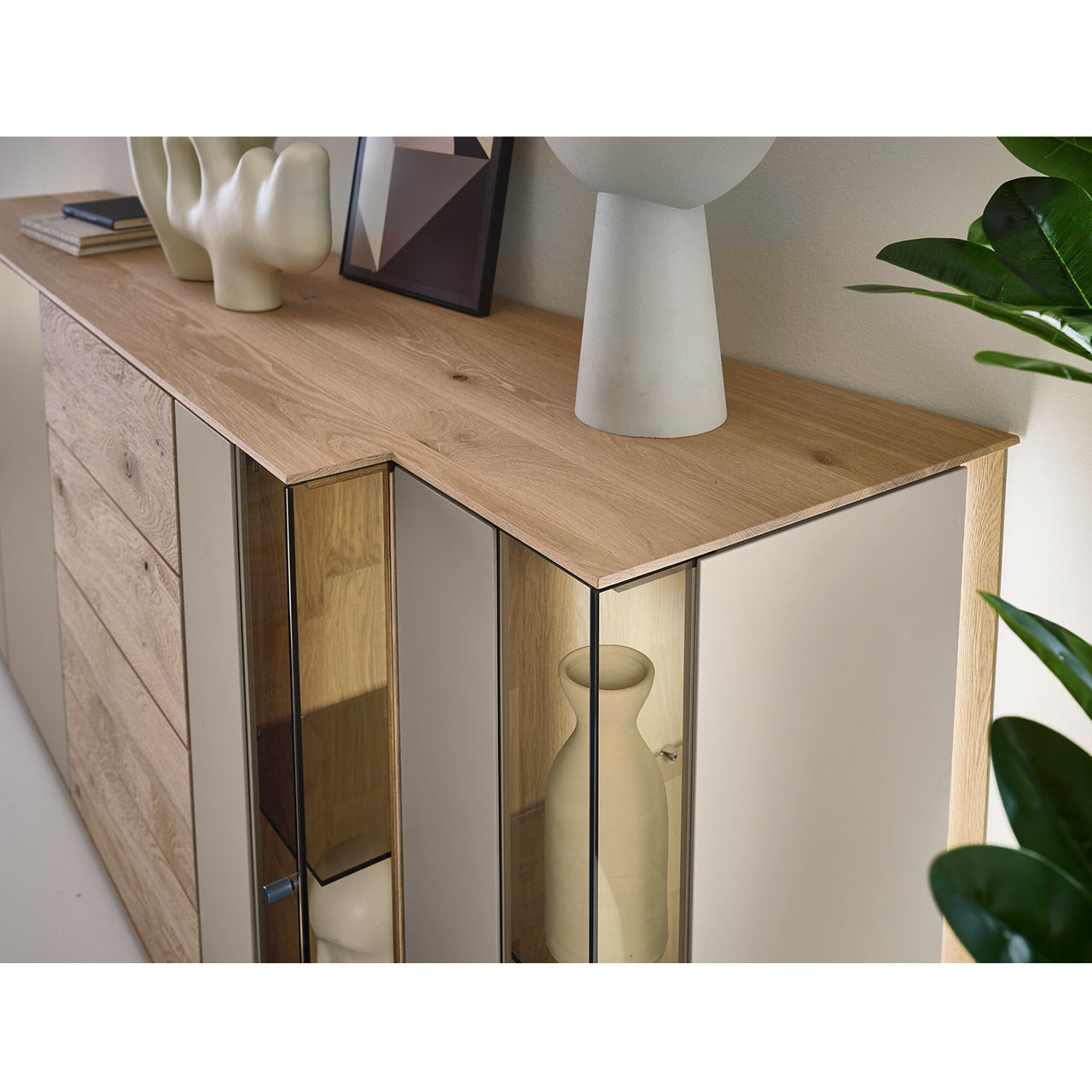 Detailansicht des modernen Sideboards SVEA Nr. 4201 aus massiver Kerneiche Natur und Lack Sand mit asymmetrischer Front aus Glas- und Holzelementen sowie dekorierter Ablagefläche.