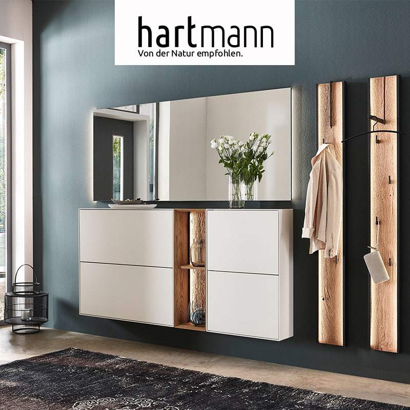 Hartmann VELKO - Flurmöbel aus massiver Birke weiß lackiert kombiniert mit Kerneiche Umato und Metall anthrazit. Ambientebild zeigt zwei weiße Schuhkipper dazwischen ein beleuchtetes Regal mit edler Holzwand, großer Wandspiegel und zwei Wandgarderoben.